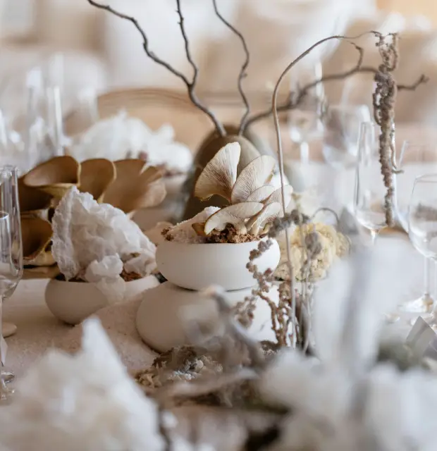 Decoración de mesa con cuencos blancos que contienen hongos, ramas secas y elementos orgánicos, acompañados de copas de cristal.