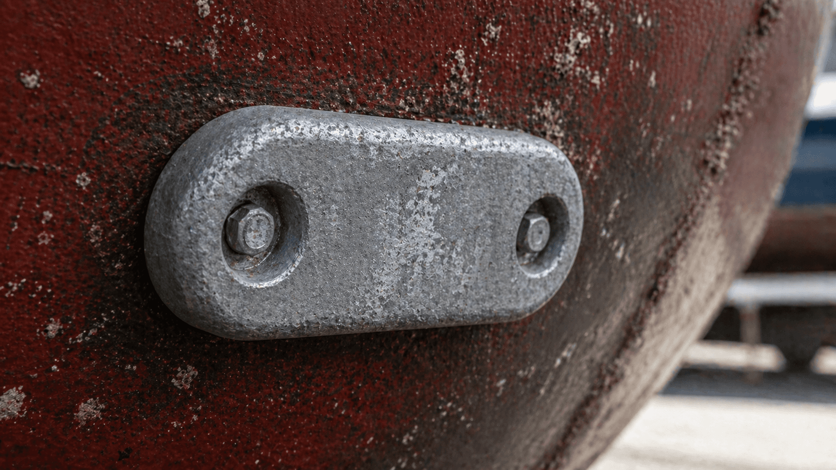 Zinc anode bolted to a boat hull with antifouling paint visible around it.