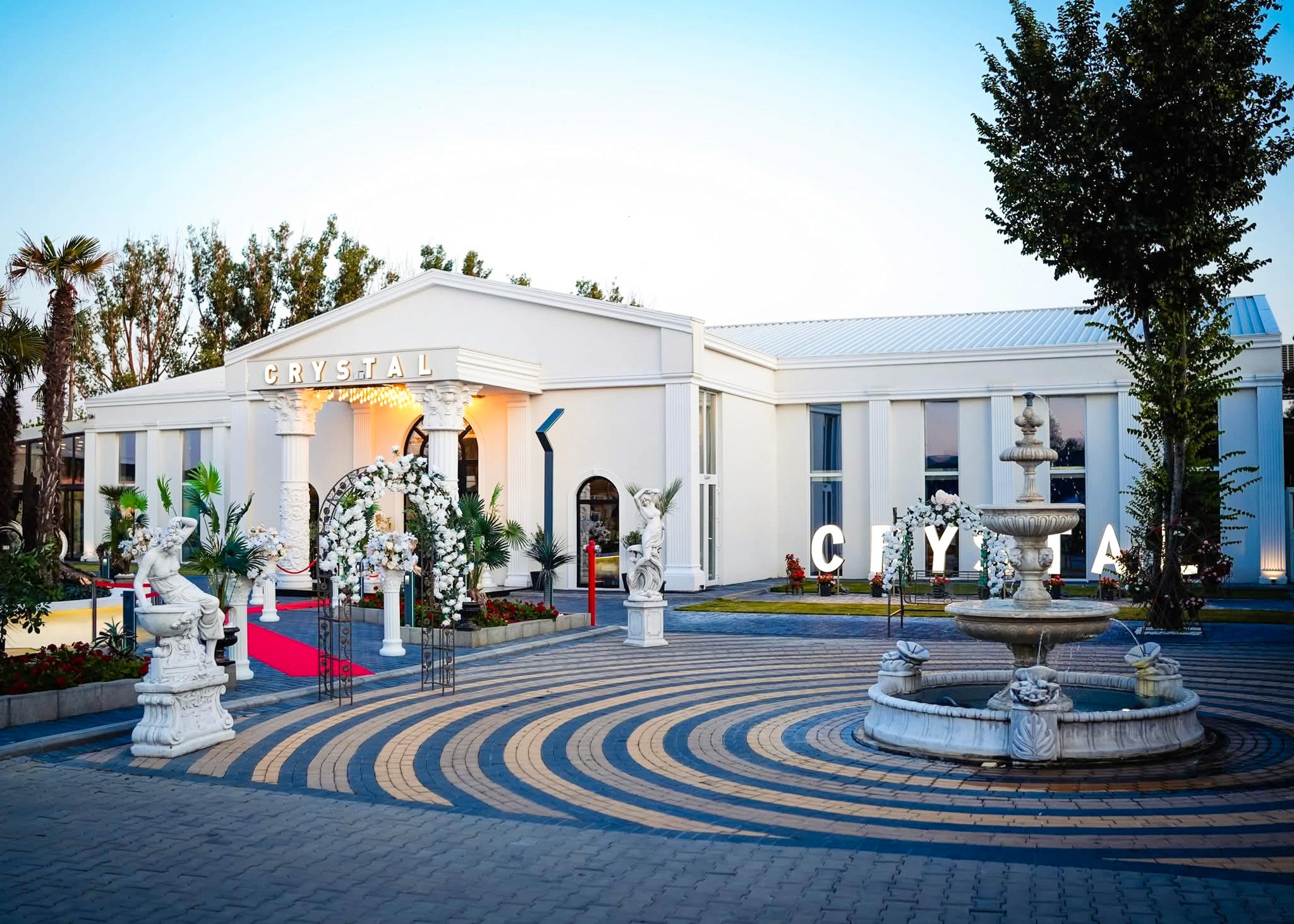 Spacious, luxurious living room with high ceilings, an elegant beige sectional sofa, warm ambient lighting, classical artwork, and rustic architectural elements, featuring an open layout with a view of a mezzanine level.