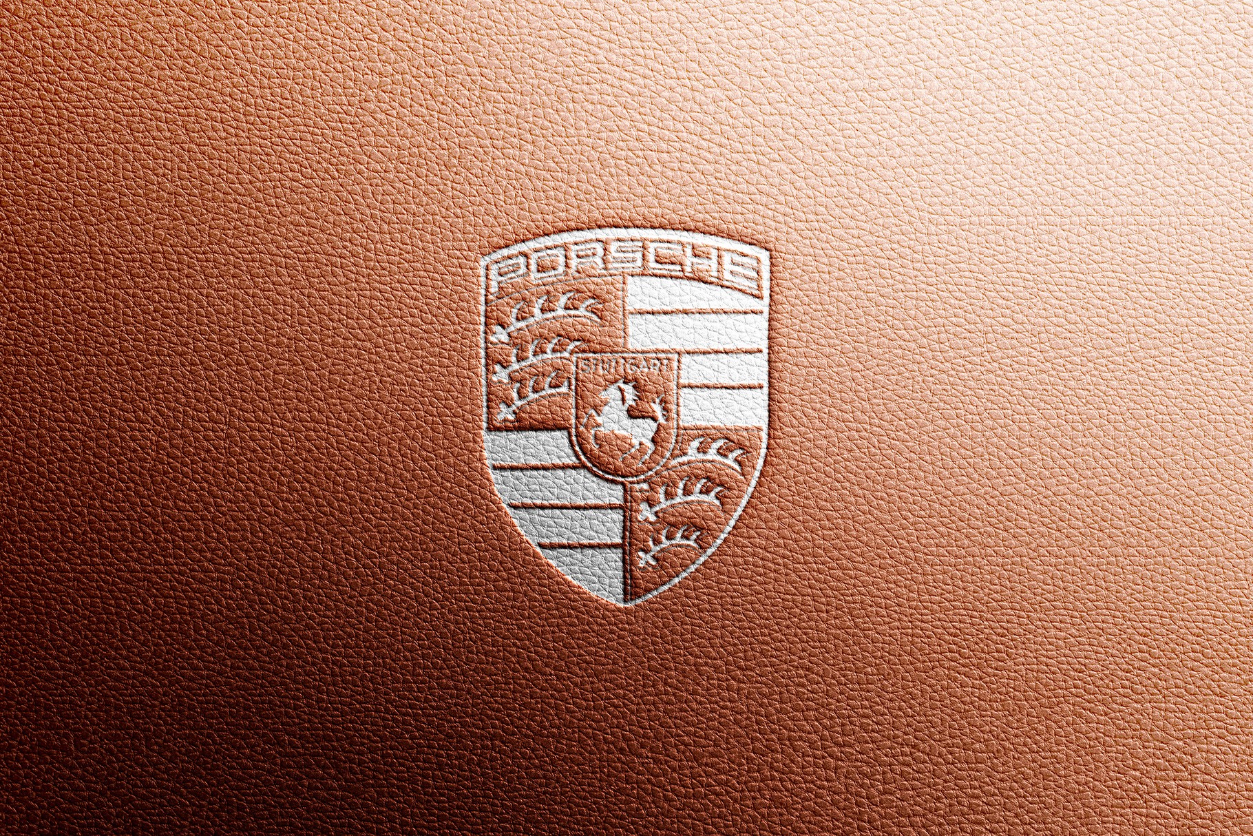 A detailed embossed Porsche crest logo mockup on the luxury brown leather.