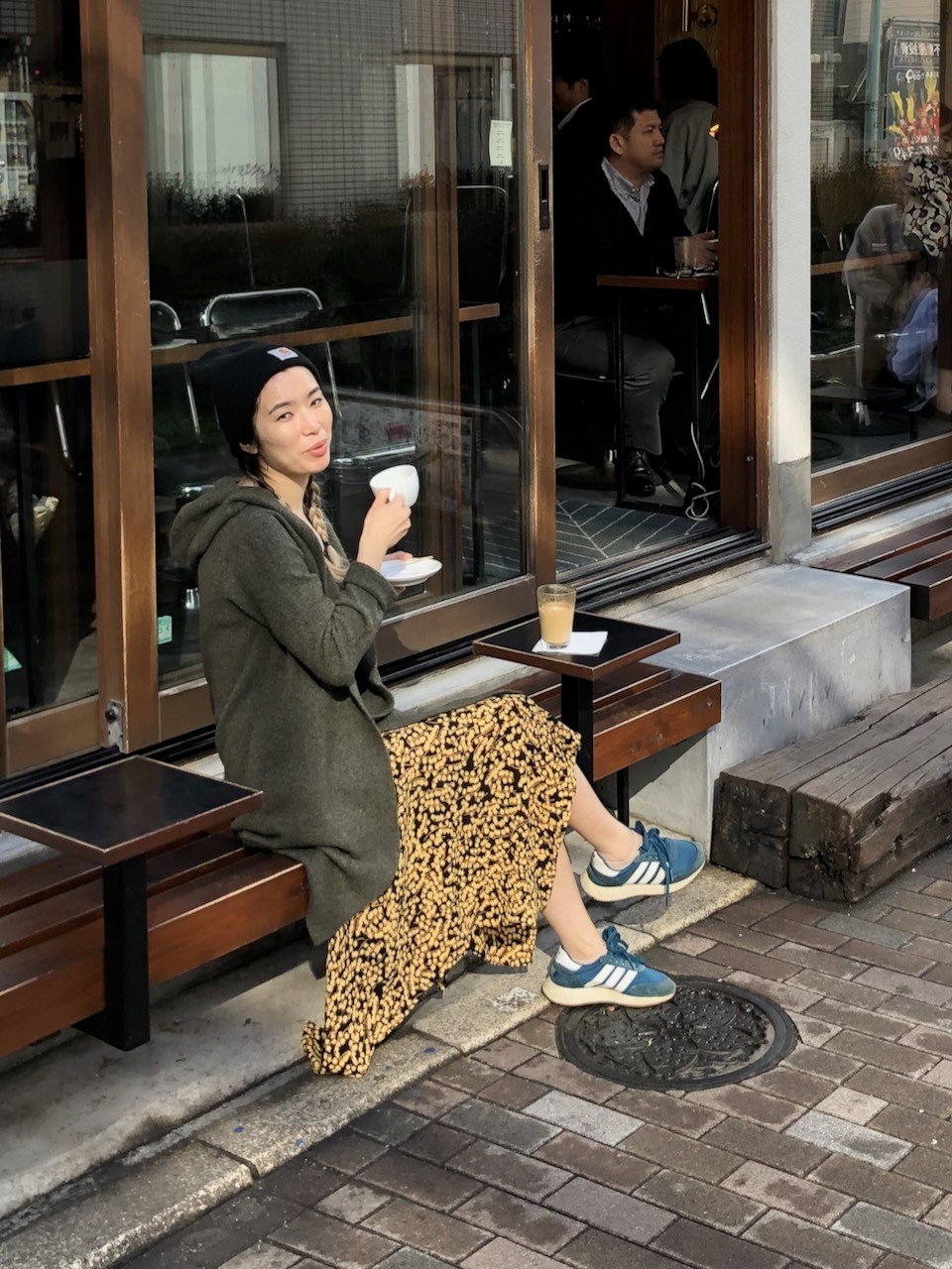 Renee holding up a cup of coffee while seated outdoors of a cafe in Japan.