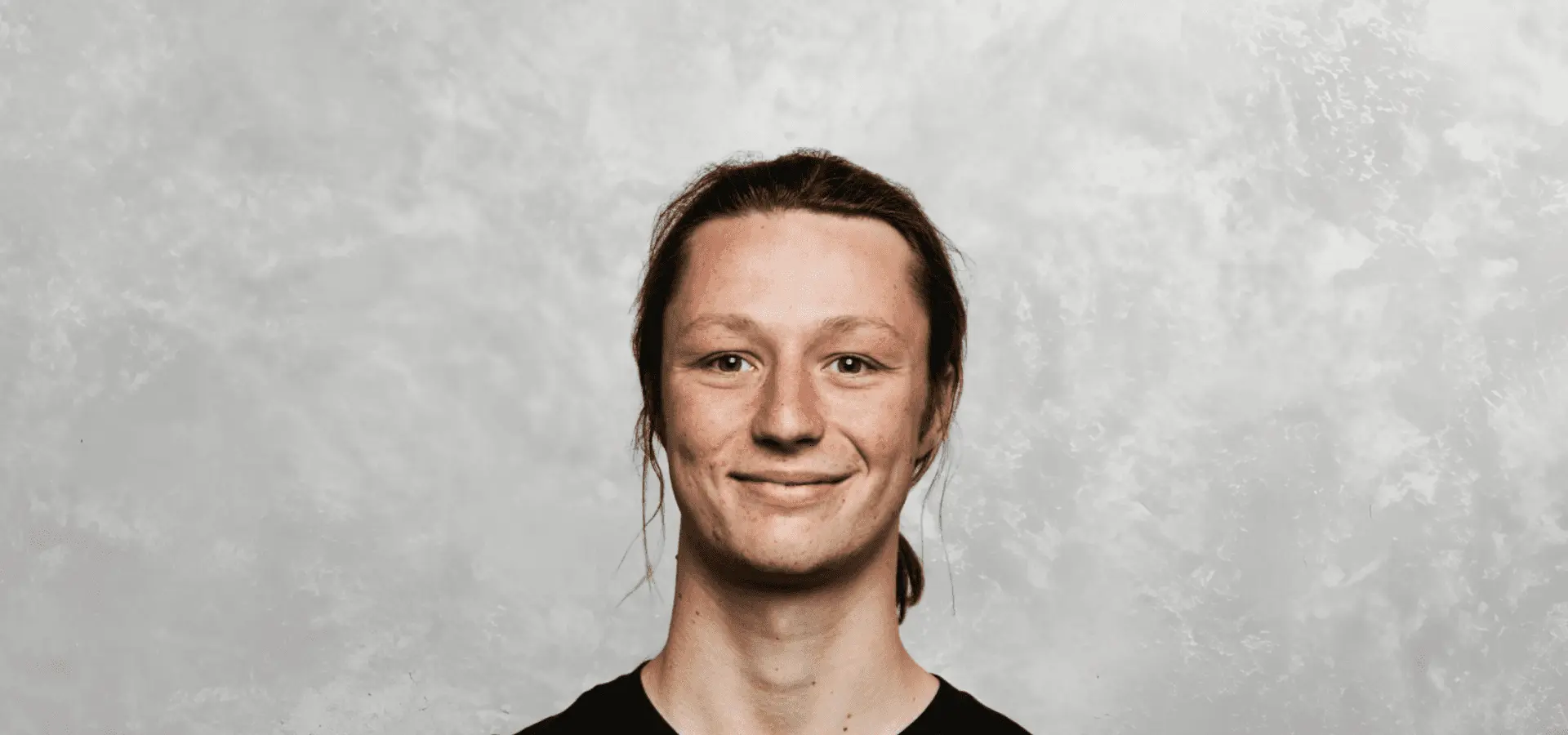 Young person with long hair smiling against a textured background.