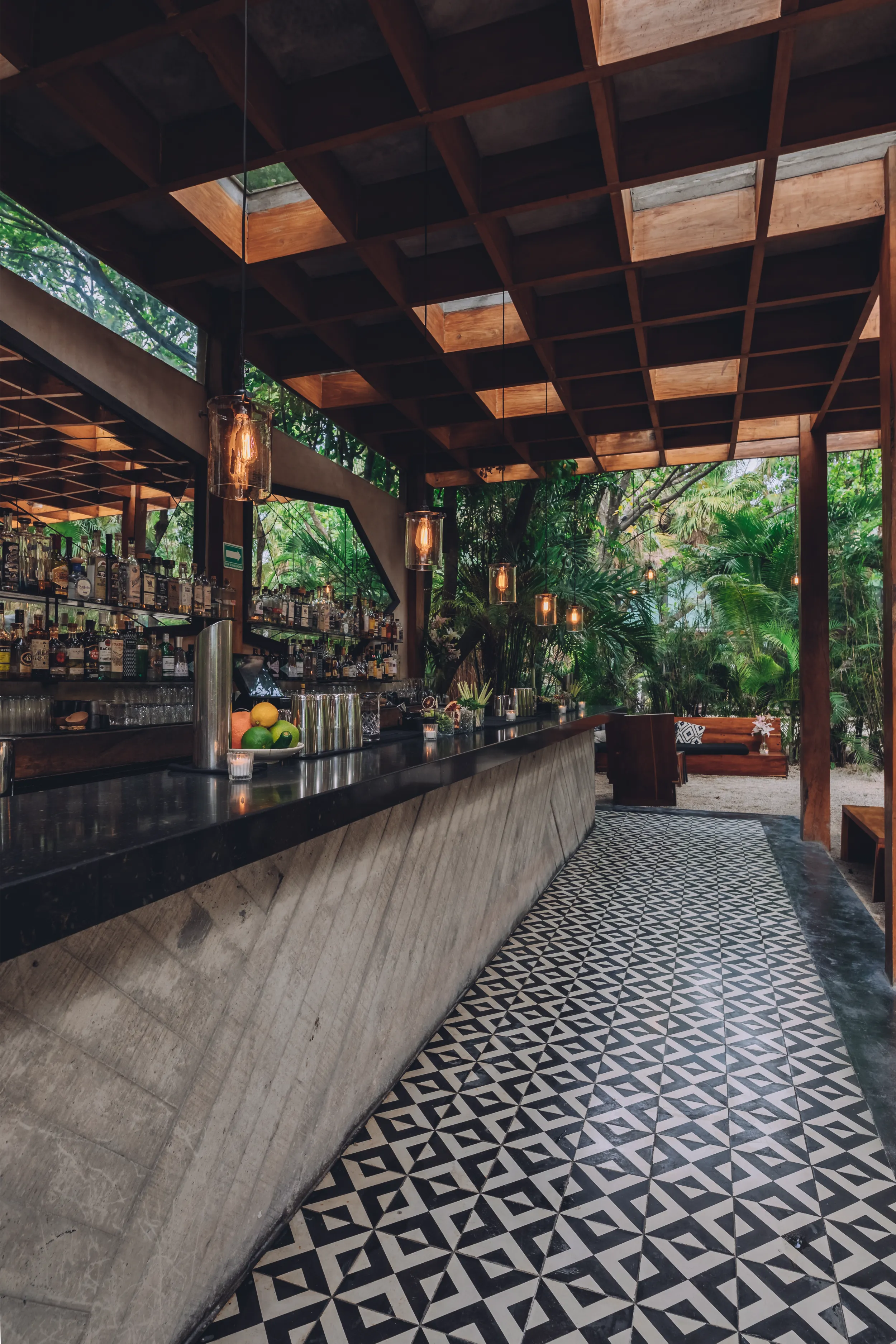 Bar design detail showcasing a raw concrete counter, black and white geometric floor tiles, and the overhead wooden grid structure.