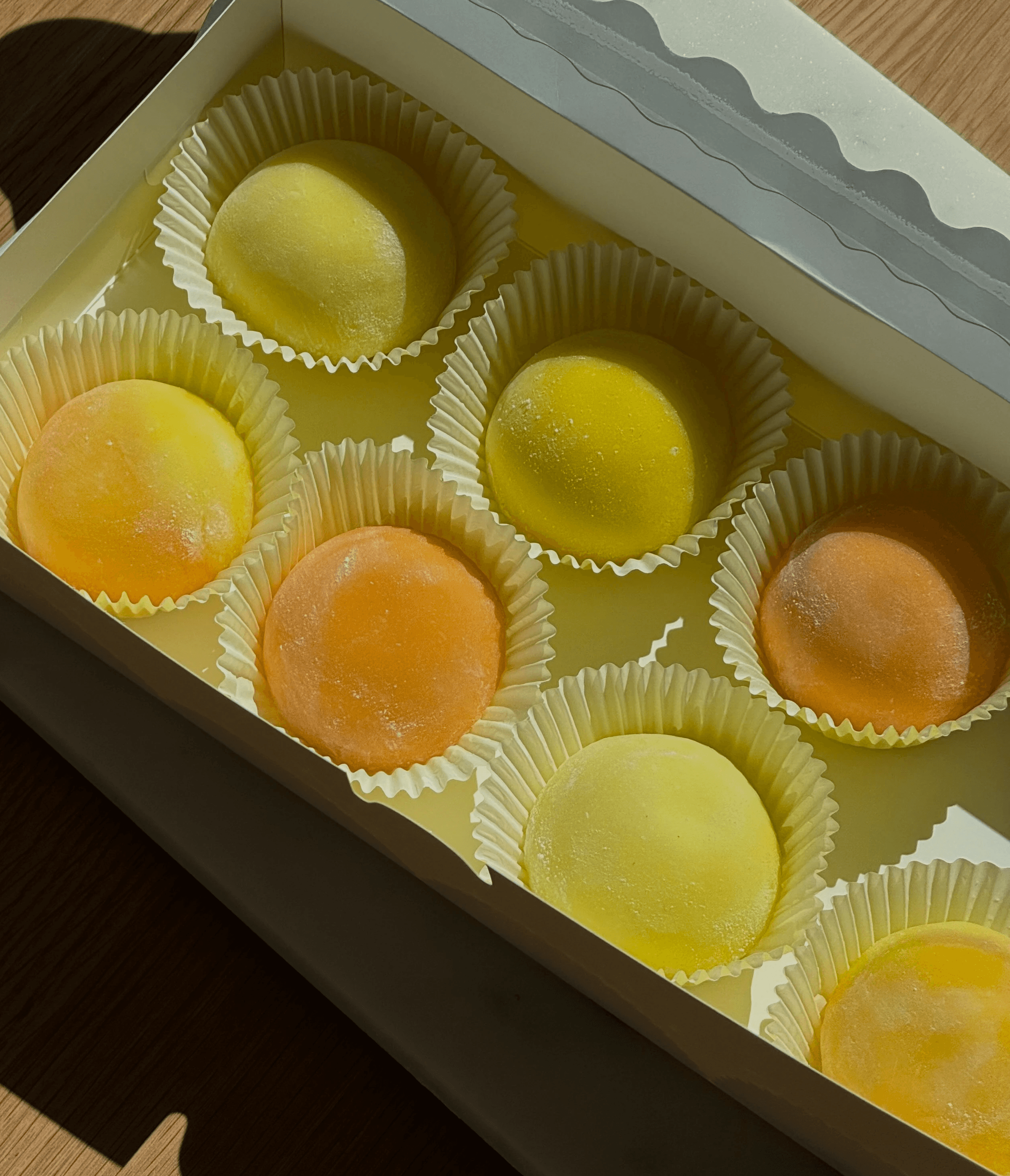 Assorted yellow and orange mochi in a box with sunlight highlighting the soft powdered surface
