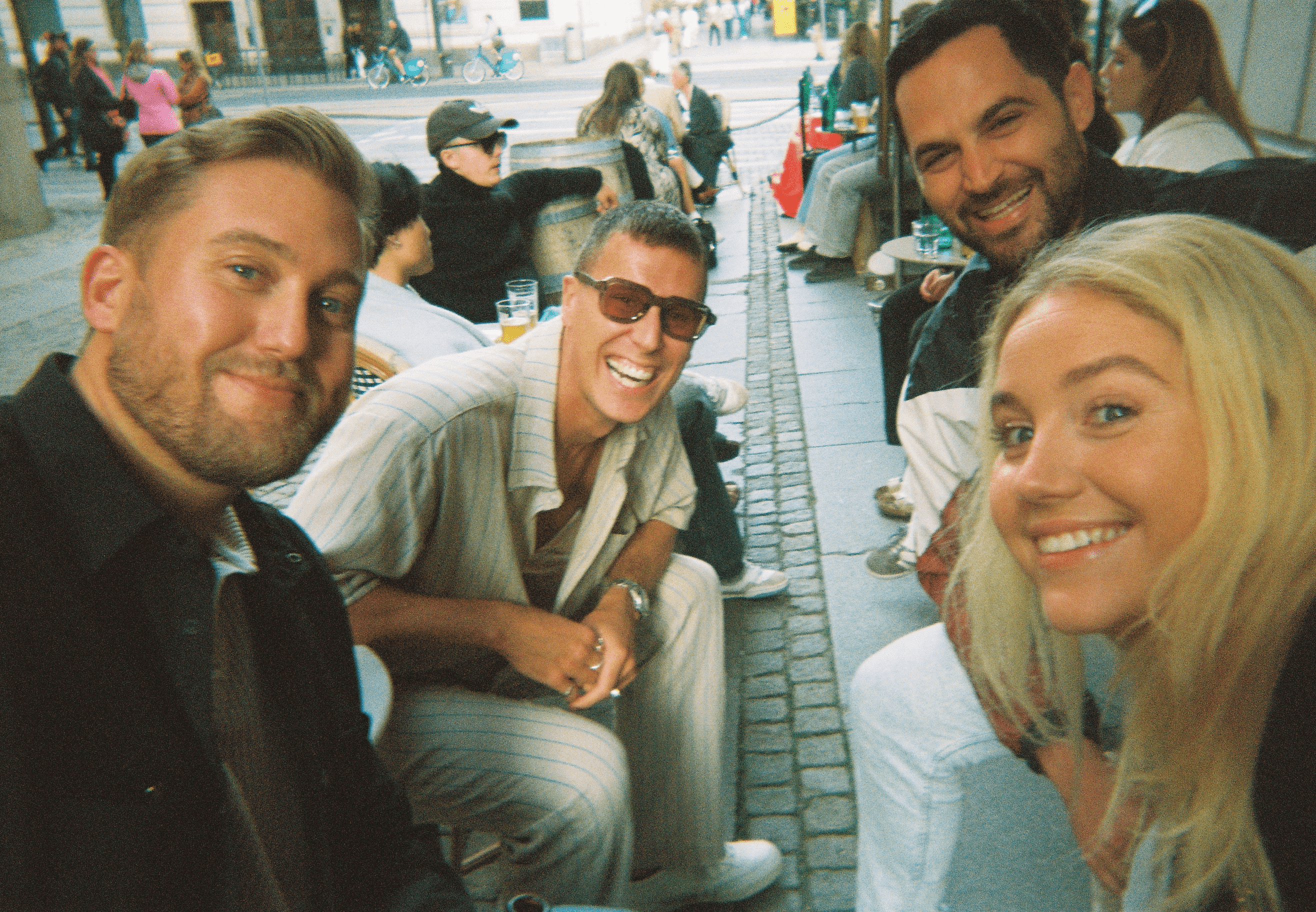 Group of people sitting outdoors at a café, smiling and posing for a photo together.