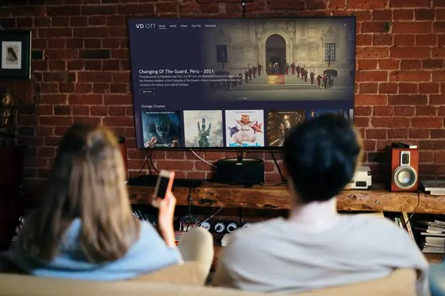 A decorative image featuring a person watching Debat Direct on her monitor while simultaneously using the Debat Direct website on her laptop