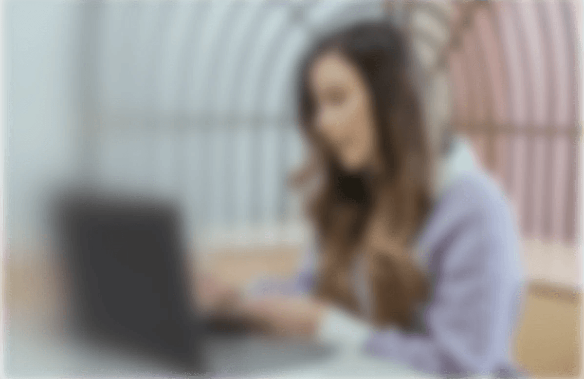 Donna seduta a una scrivania lavora al computer portatile, in un ambiente luminoso con sfondo colorato e struttura ad arco.