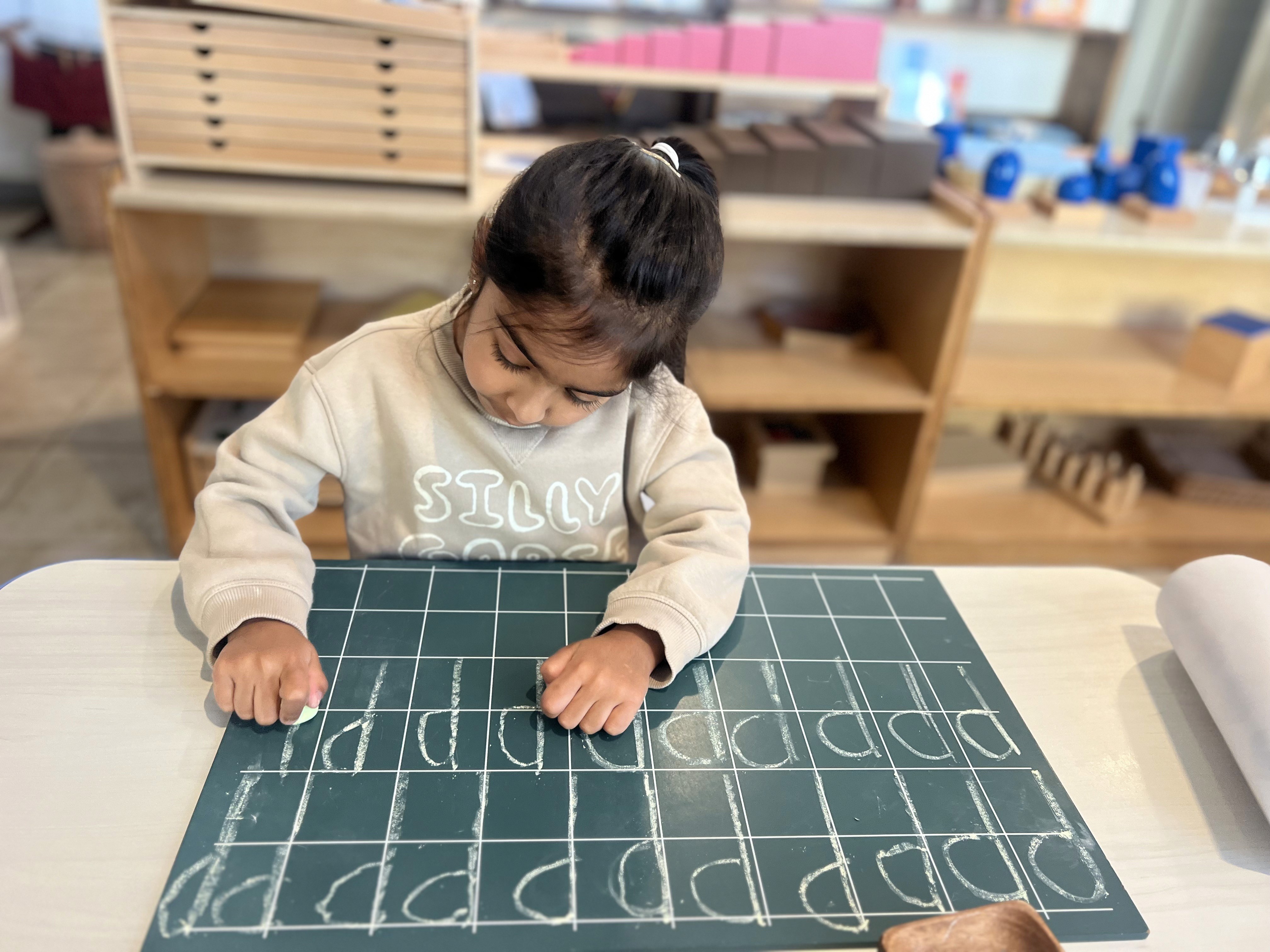 Montessori preschool child tracing letters on chalkboard in Early Childhood classroom in Irvine CA