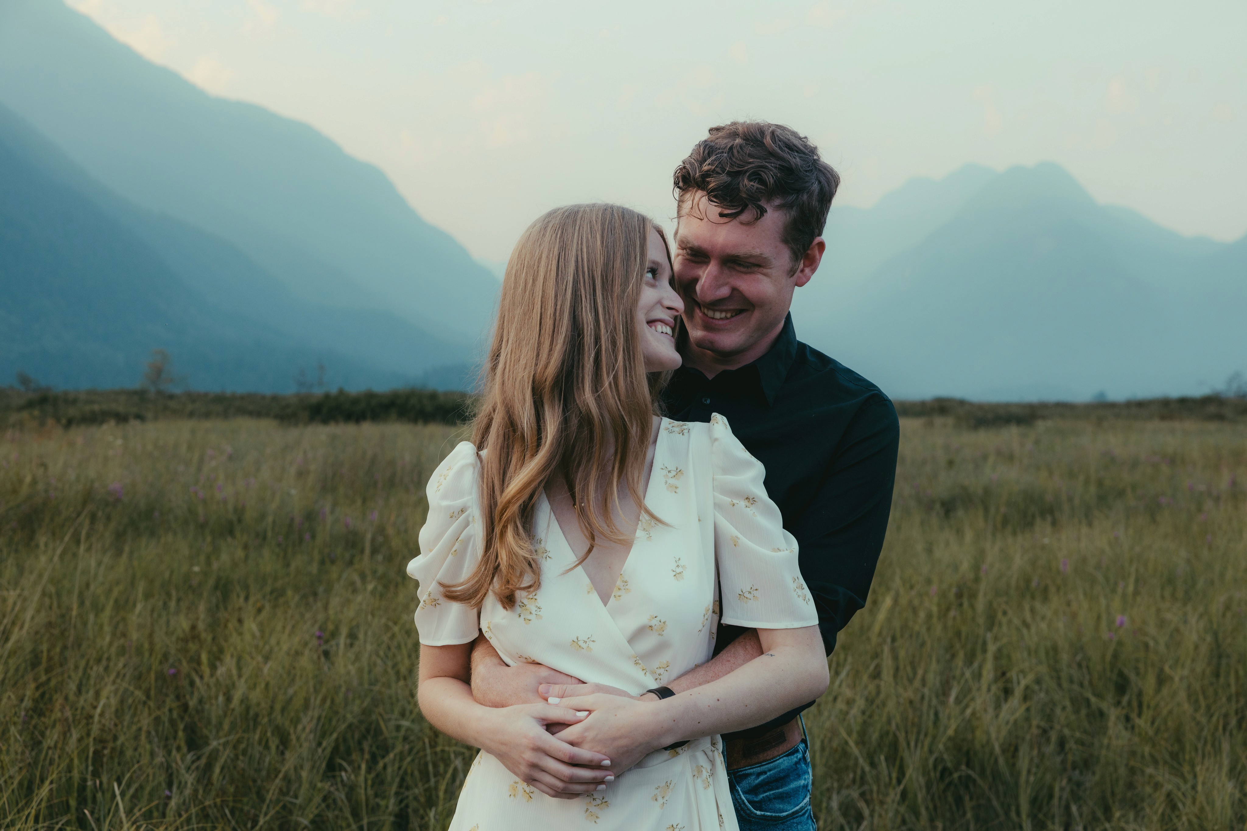 Justin hugging Roxy from behind in a grassy valley with misty mountains