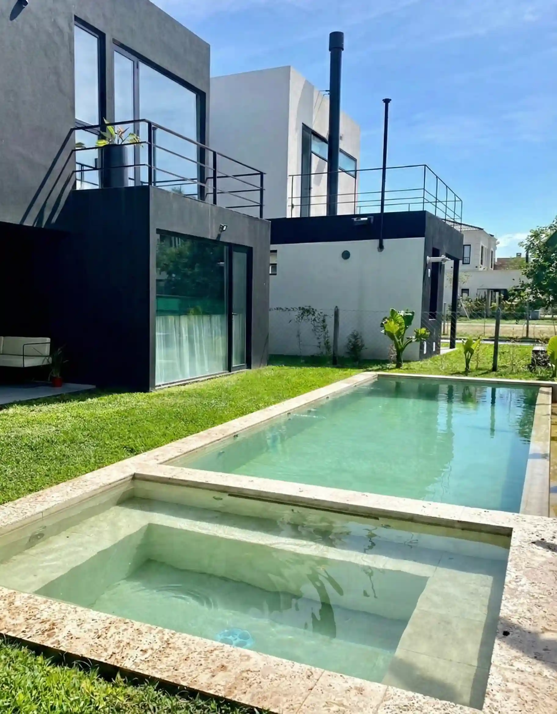 Pileta de hormigón arquitectónico con sector de hidromasaje cuadrado integrado, ubicada en el jardín de una casa de estilo minimalista.