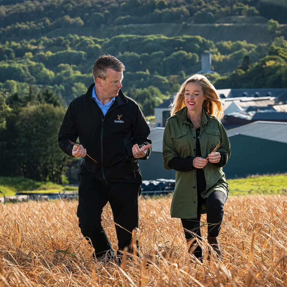 Woman and man walking in field, whisky distillery in background