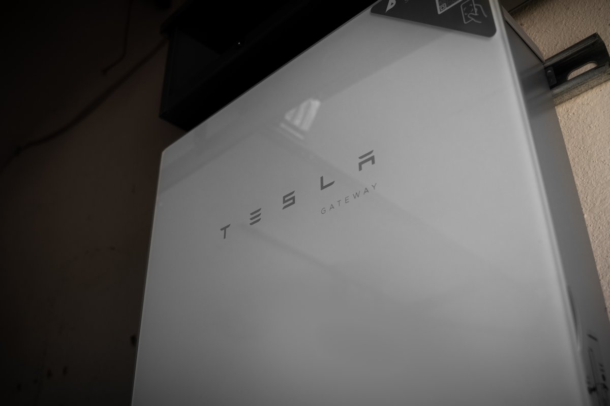 A home battery mounted on an exterior wall beside a garage