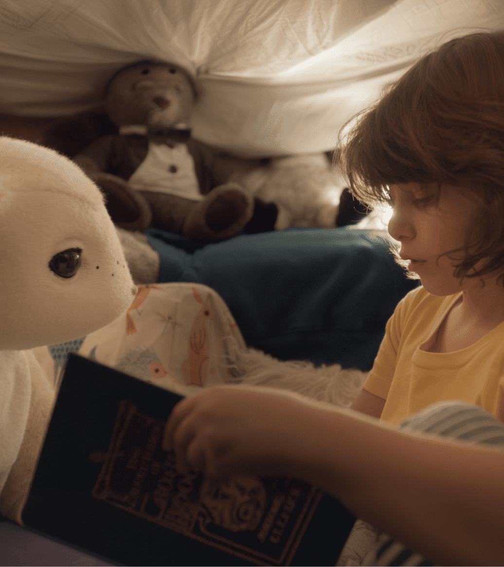 Child reading a book in bed by lamplight with a familiar