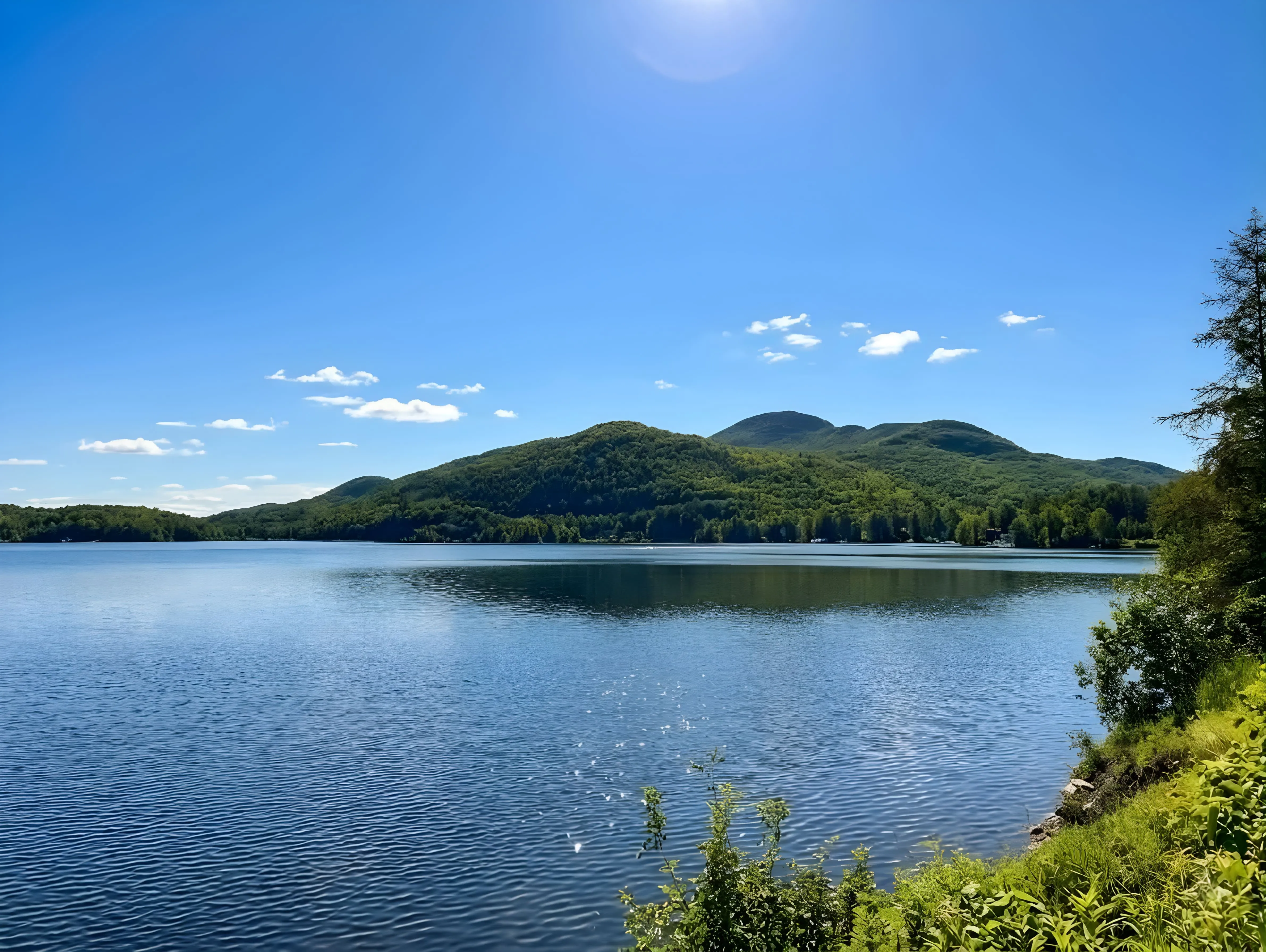 Vue panoramique du lac Orford entouré de collines boisées sous un ciel bleu clair, à Austin en Estrie, Québec.