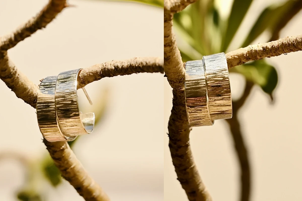 קומפוזיציה אמנותית של עגילי חישוק מכסף בעבודת יד, תלויים על ענף עץ יבש תחת אור שמש טבעי. התמונה מבליטה את הטקסטורה המחוספסת והייחודית של הכסף על רקע טבעי רך, מאת Shiriz Photography הצלמת שירי עציץ.