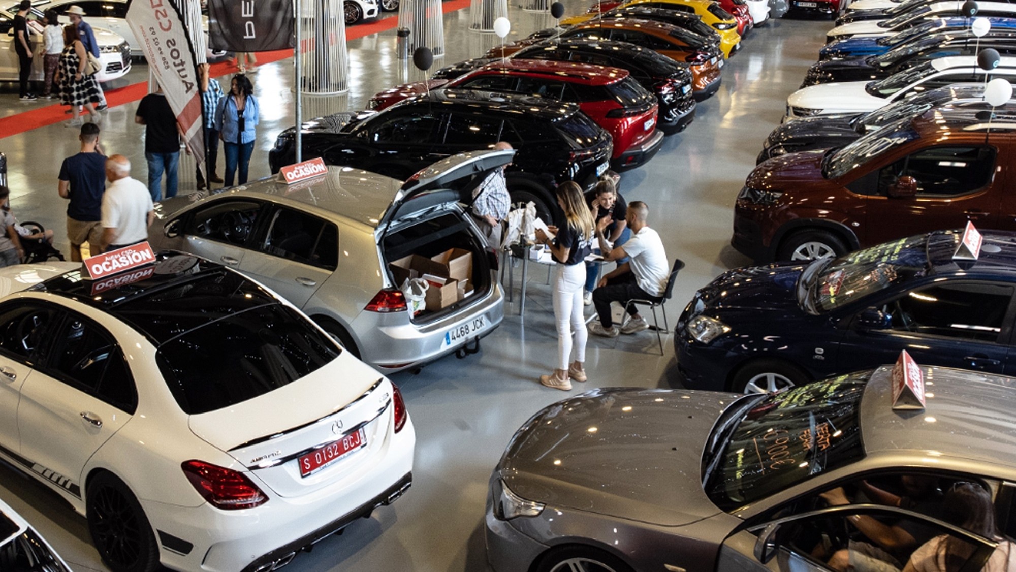 Autosalone con una varietà di veicoli in esposizione, con potenziali acquirenti che osservano.