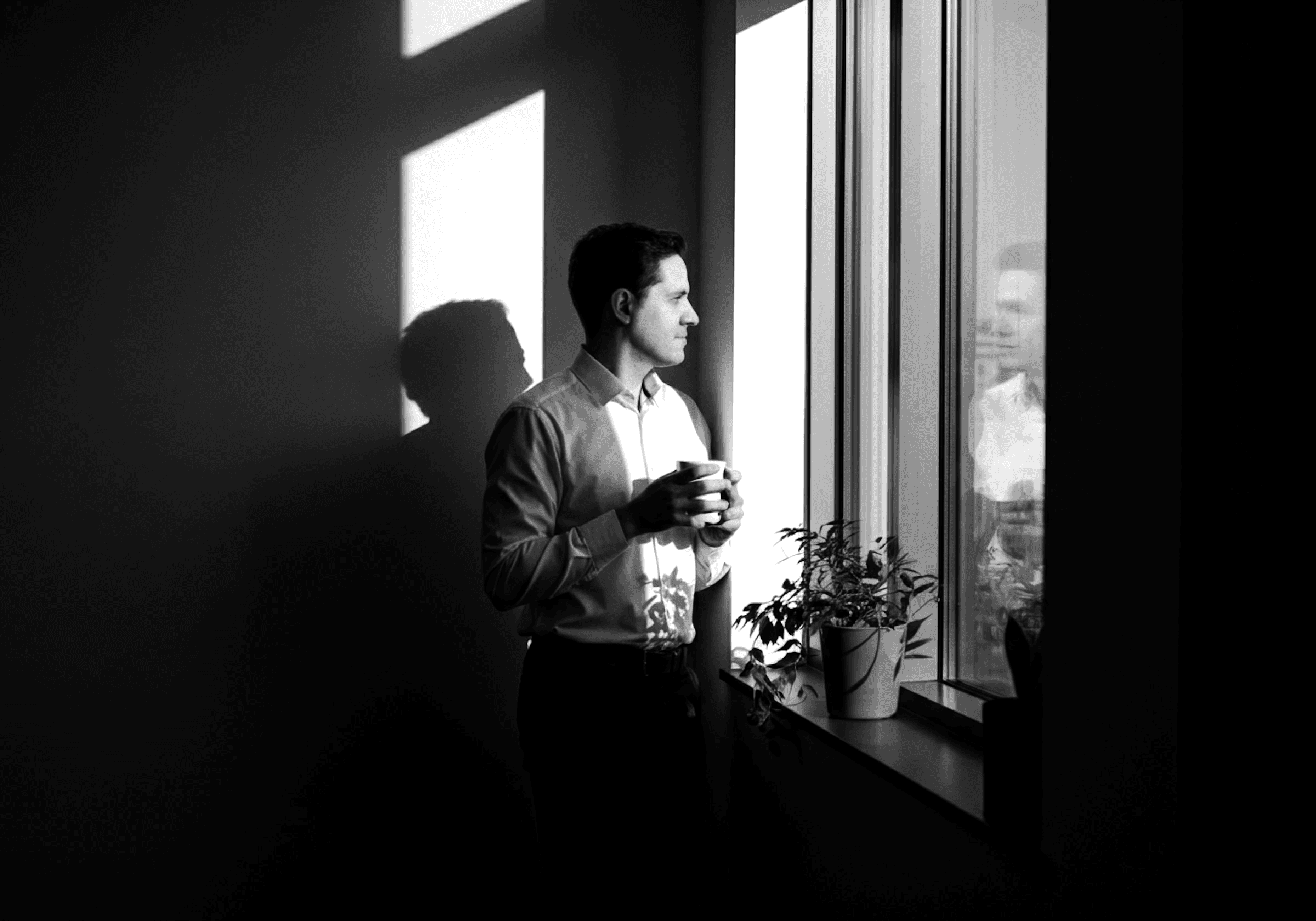 A man is standing in an office, looking out the window.