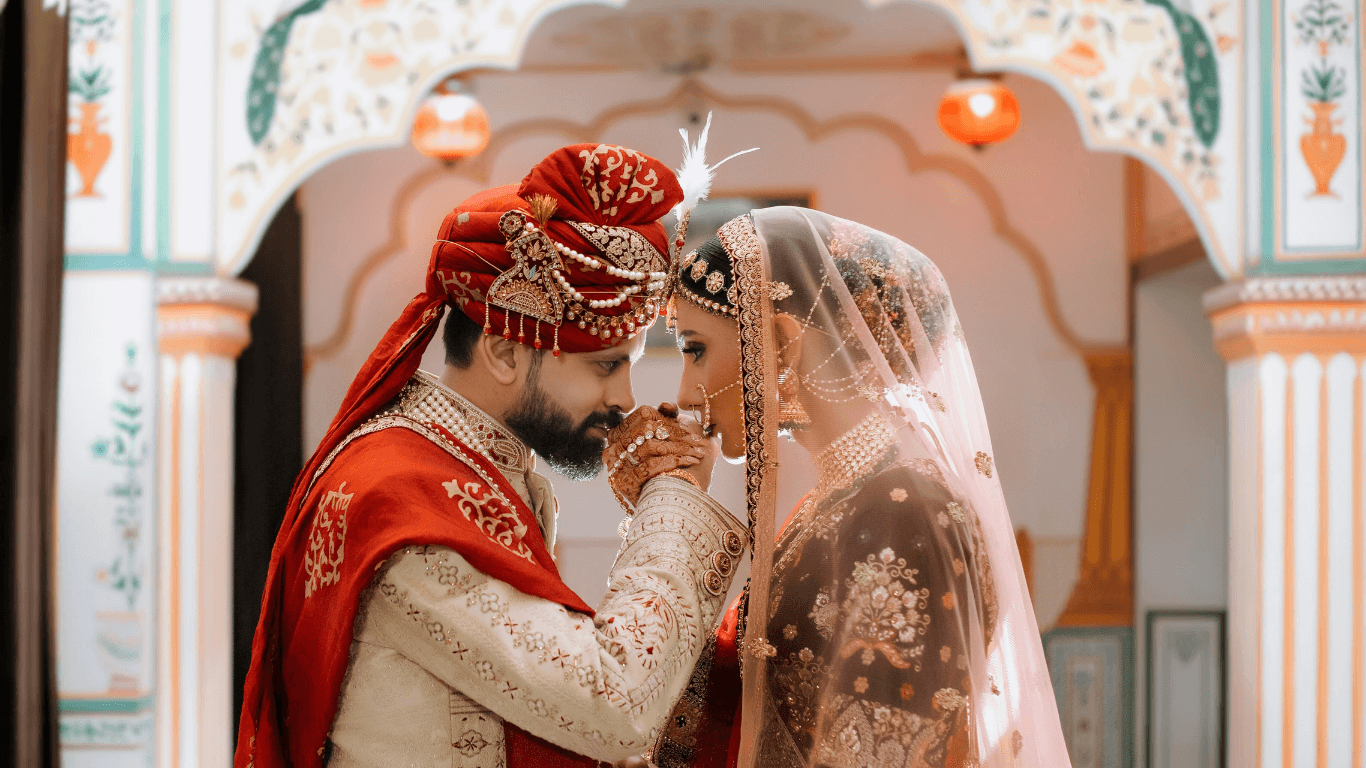 A couple in traditional wedding attire shares an intimate moment in a beautifully decorated architectural setting.