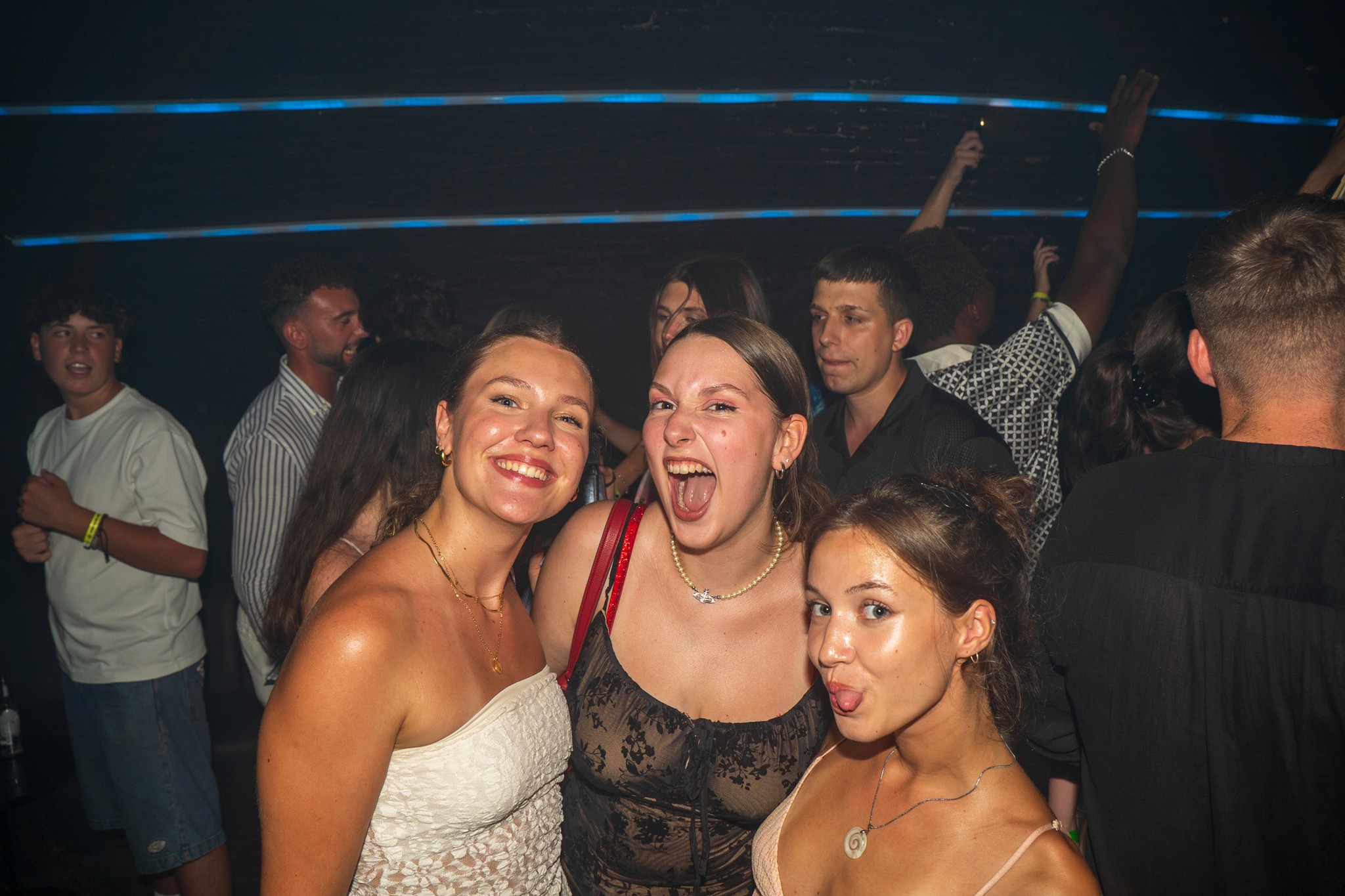 A group of women walking together at night in Nice city center, smiling and talking under street lights near busy bars.