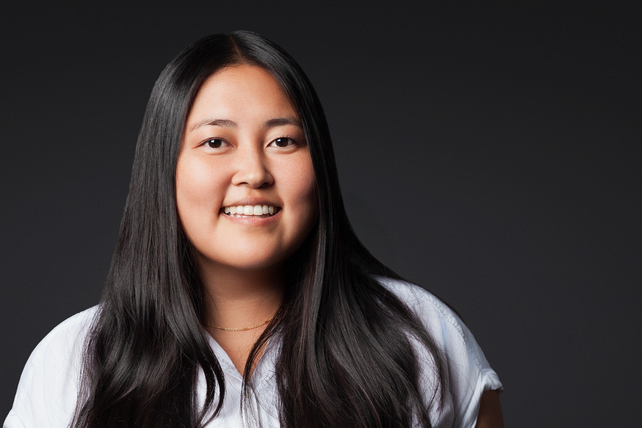 Executive branding portrait of a professional woman smiling against a dark studio background, photographed with soft, natural lighting.