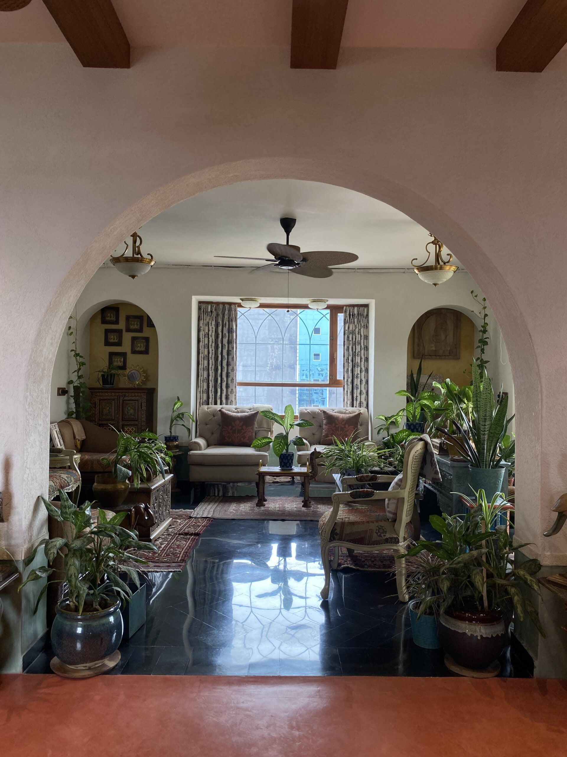 Light and depth: The glossy dark flooring reflects the natural light streaming through the large window, adding depth to this layered, heritage-inspired room.