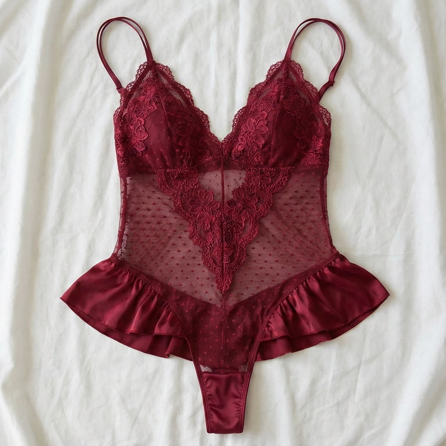 Burgundy lace bodysuit laid flat on white fabric.