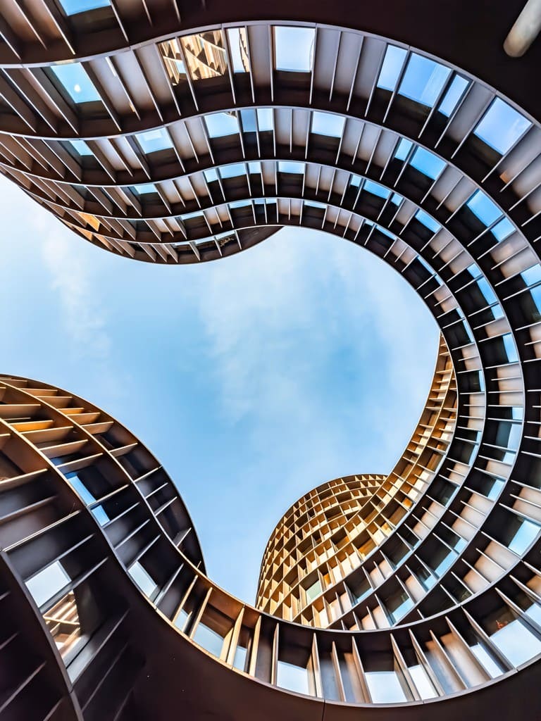 op-down view into a curved architectural atrium with grid-like windows against a blue sky.