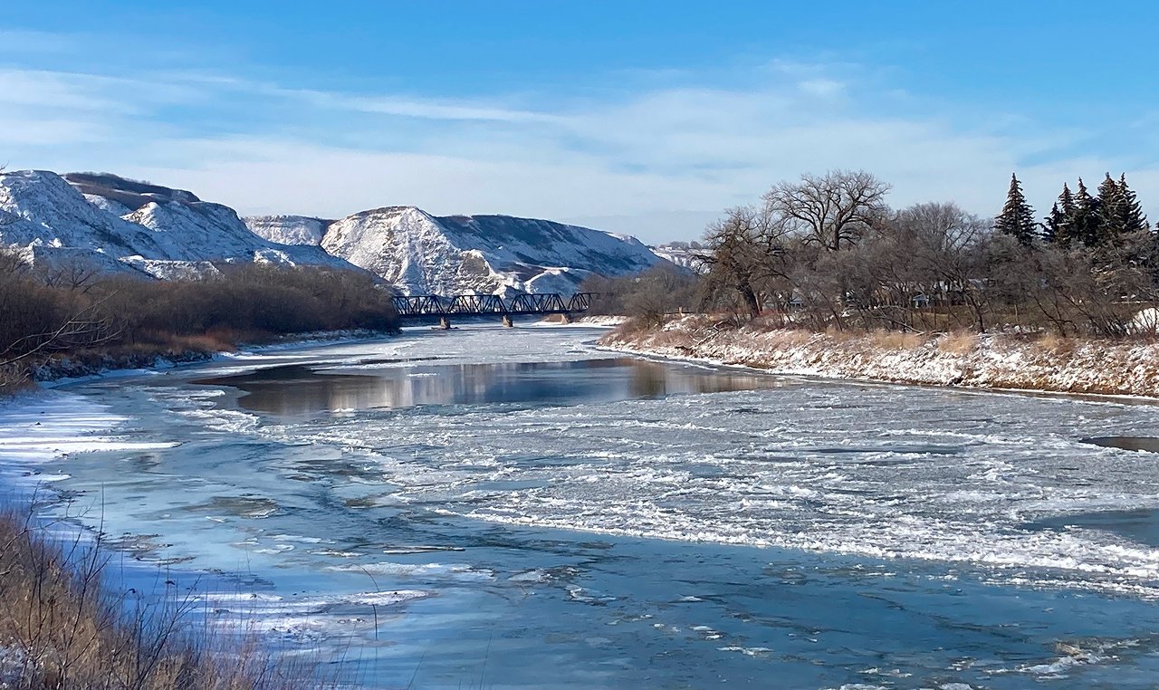 Ice-covered Red Deer River with railway bridge and badlands backdrop in winter at Drumheller