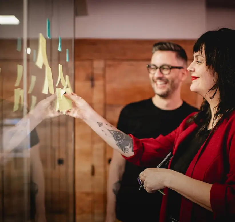 Duas pessoas interagem com uma peça em exposição, uma apontando e a outra observando, em um ambiente com iluminação aconchegante.