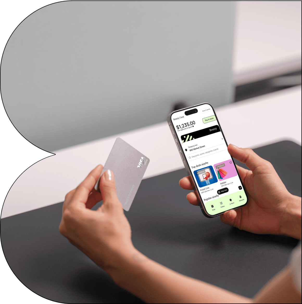 A close-up of a hand holding a credit card in front of a laptop, with another hand using a smartphone displaying a financial app. The app screen shows a digital Breezy card with a balance of $16,058.94, highlighting the availability of both physical and digital cards for seamless transactions.