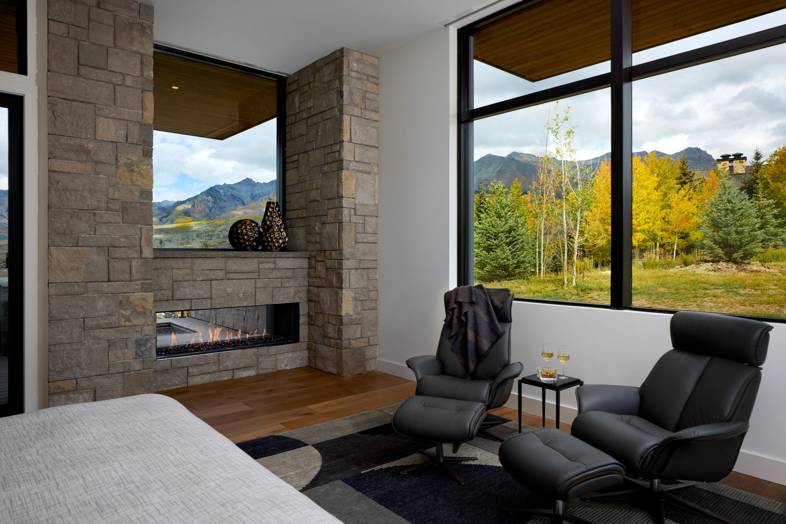 Modern master bedroom chairs near fireplace overlooking autumn trees and mountains