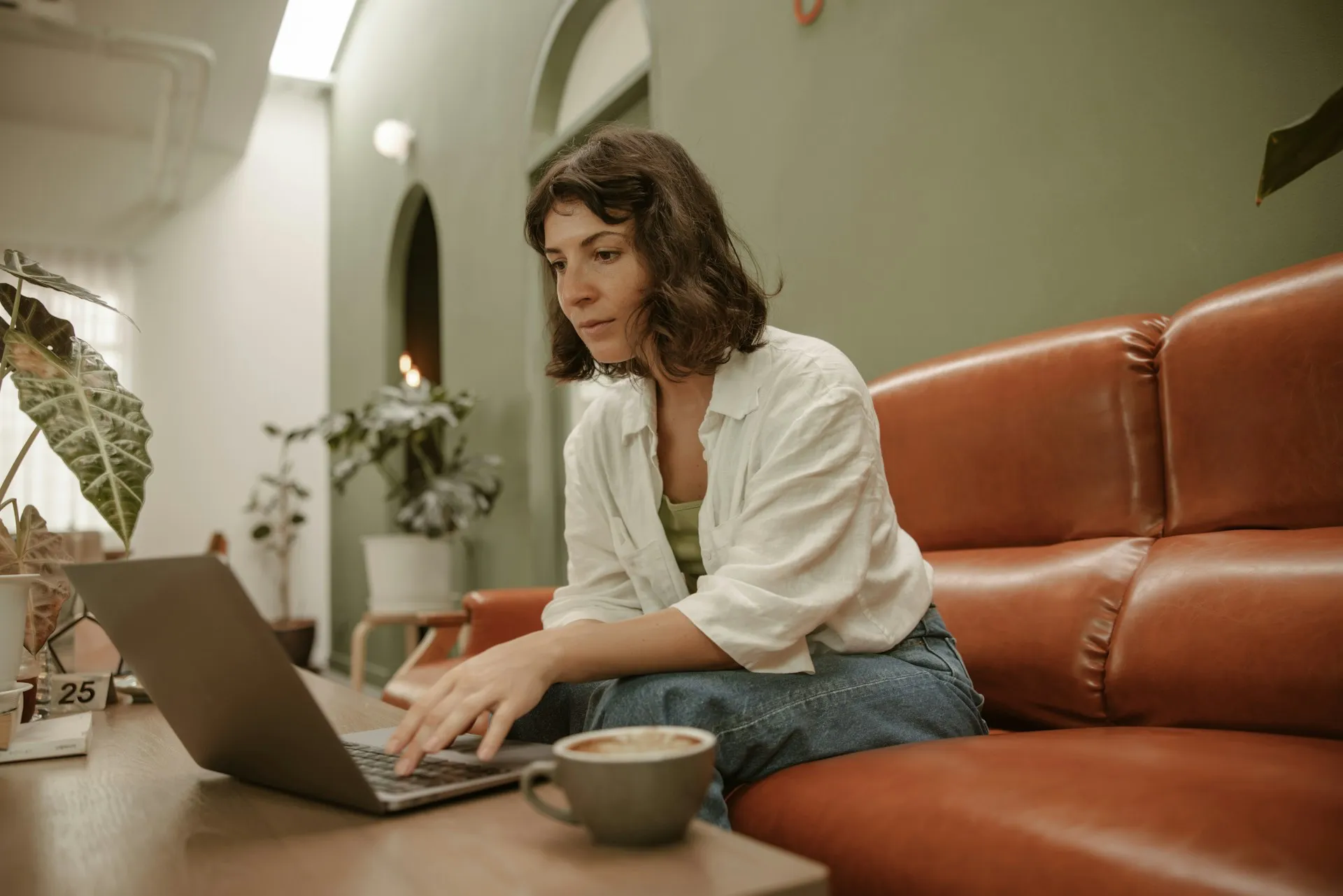 Woman sitting on a leather sofa using a laptop in a modern interior, representing focused website browsing and desktop user experience at home.