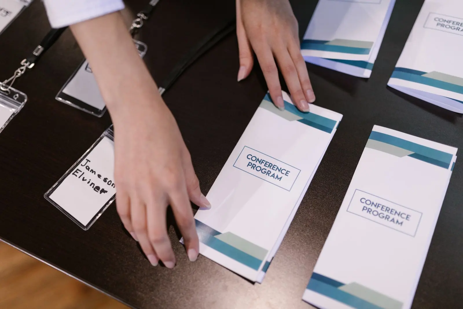 Hands laying out conference programmes and name badges on a registration desk
