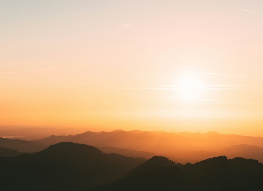 Sunset over silhouetted mountain ranges with pastel sky.