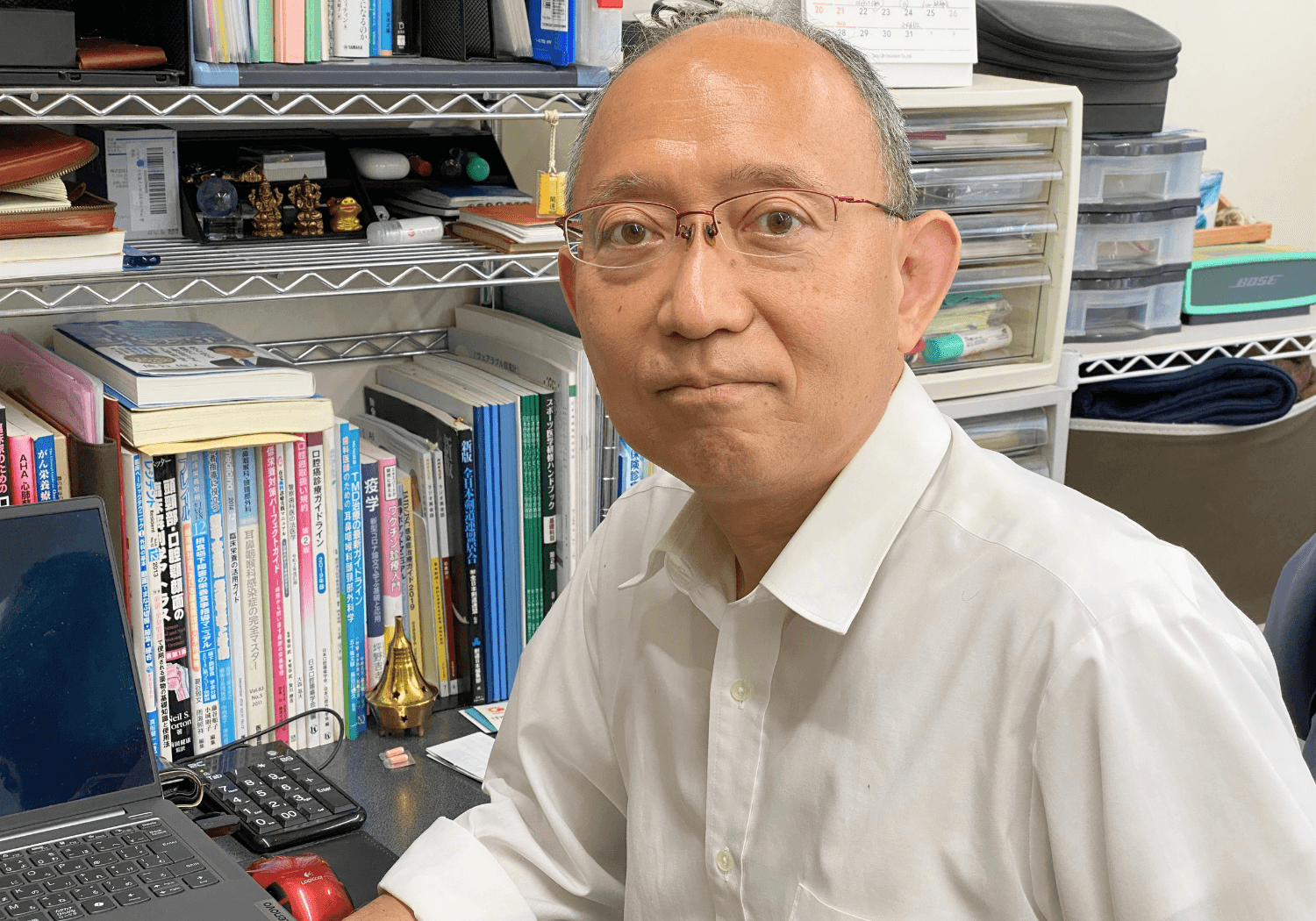 デスクでカメラを見つめる若菜康弘先生