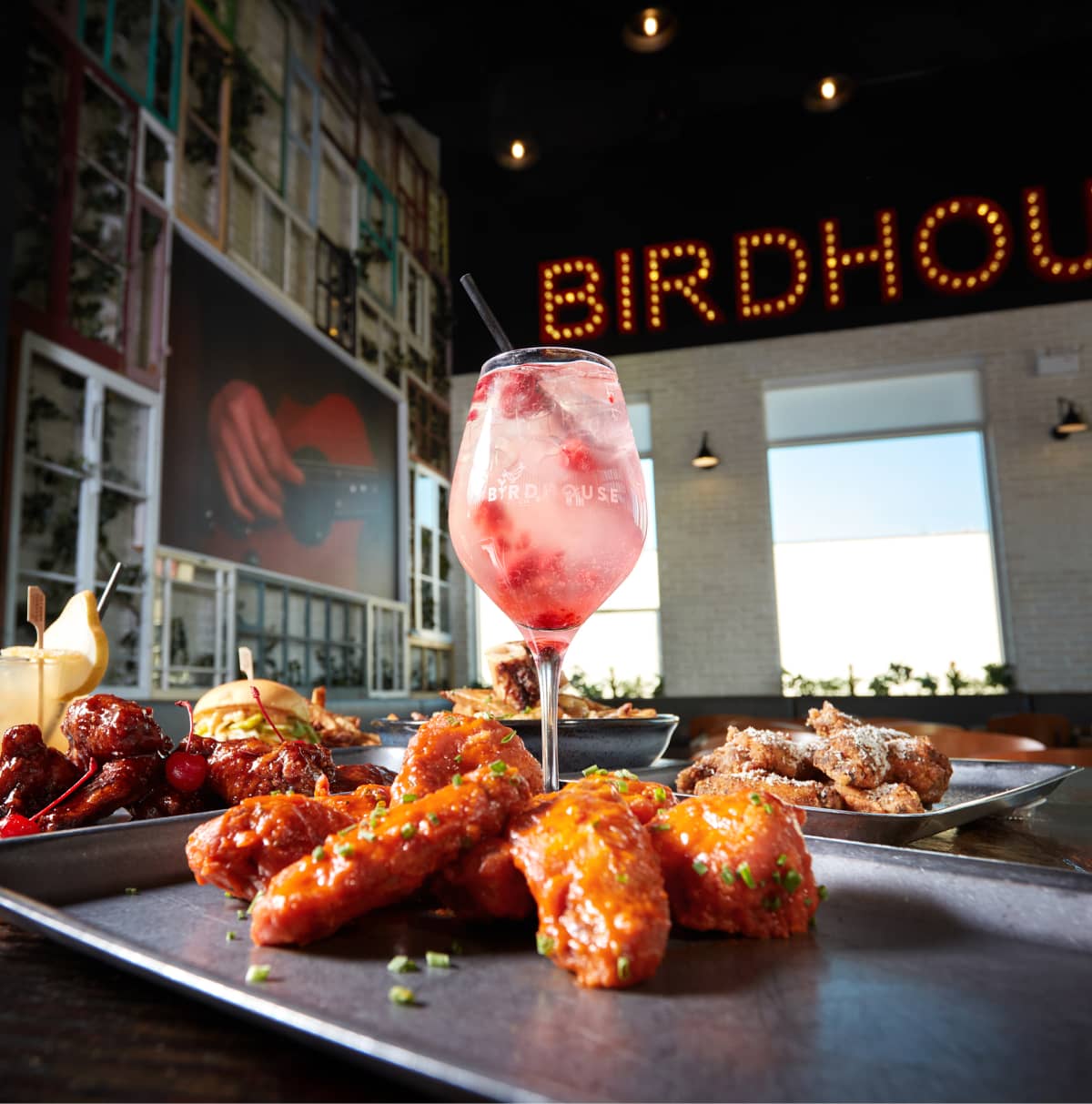 Ailes de poulet dans une assiette devant un verre de cocktail dans le restaurant Birdhouse