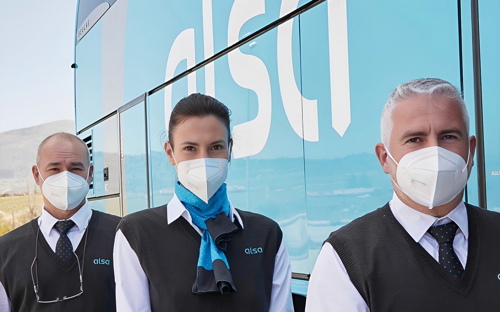 Personal de Alsa en uniforme con mascarillas junto a un autobús en el Aeropuerto de Granada.