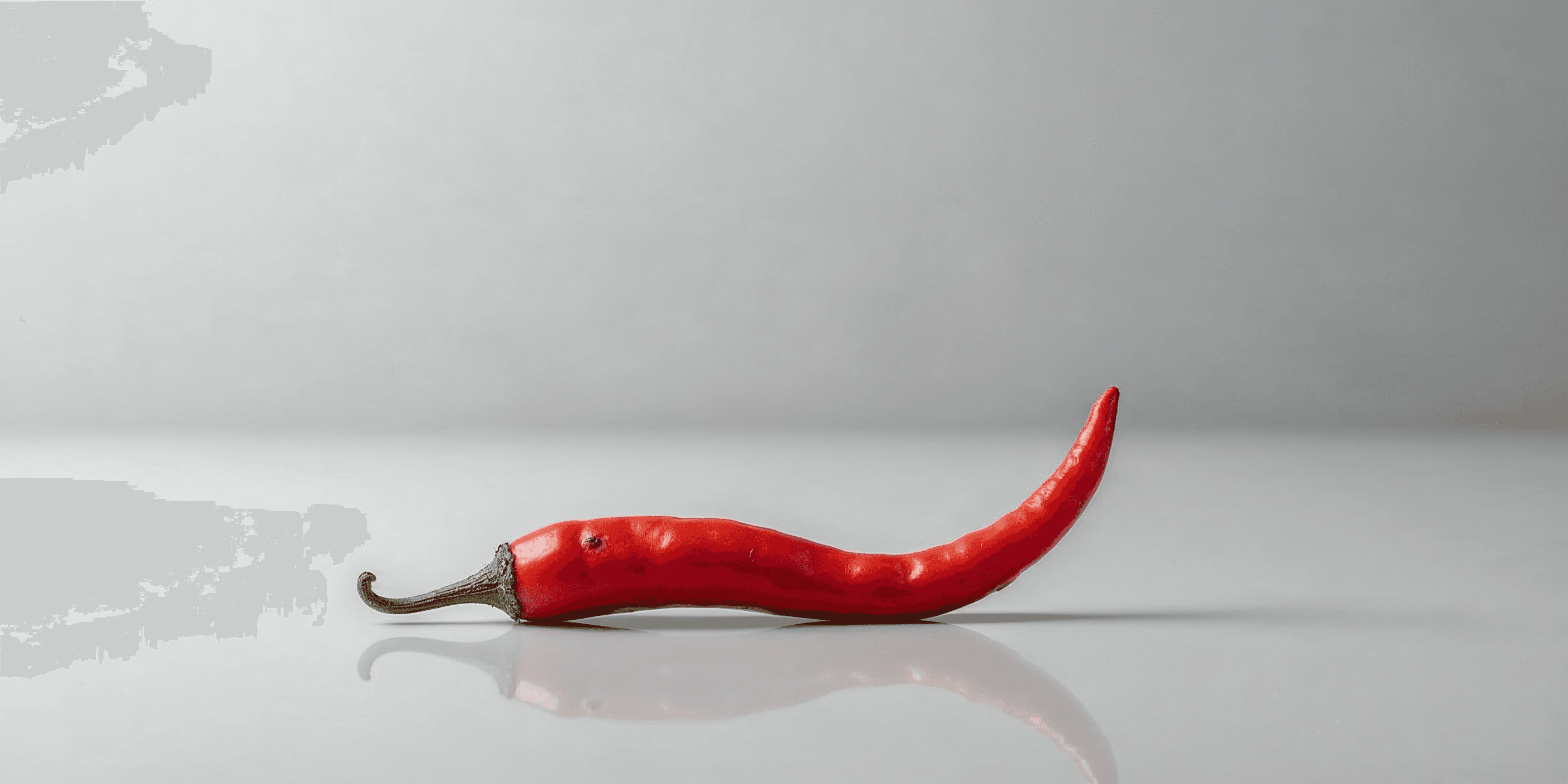 curved red chili pepper on a pale surface with subtle reflection