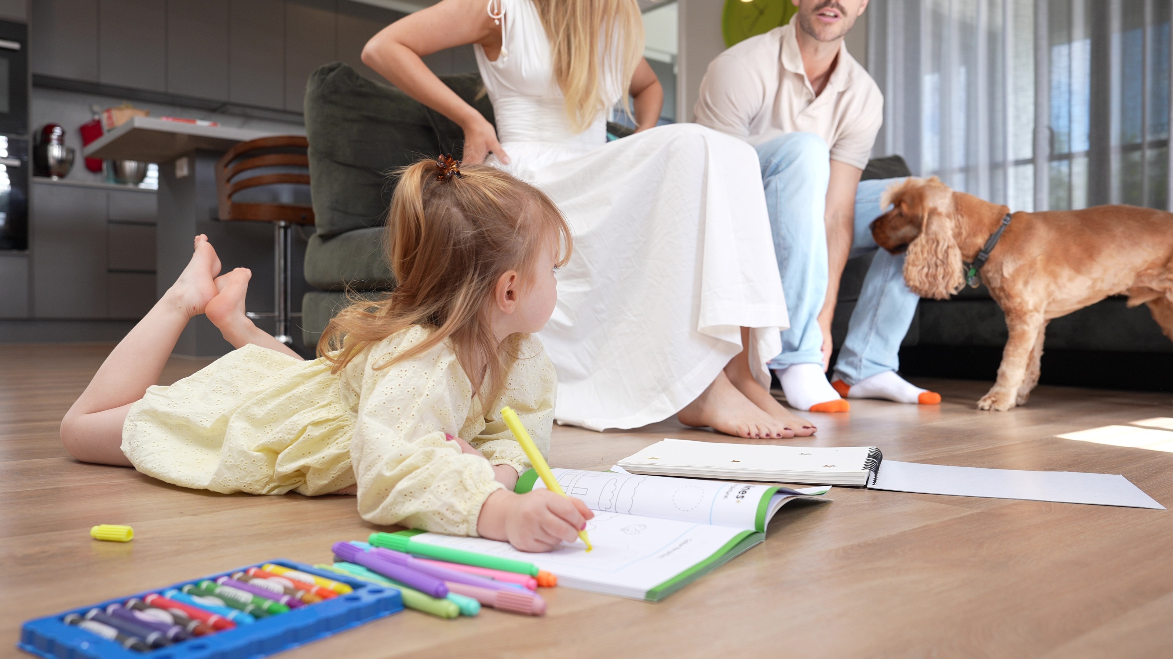 Young child drawing on hybrid flooring while the family and dog enjoy the living space, creating a warm, comfortable floor built for everyday Queensland family moments.