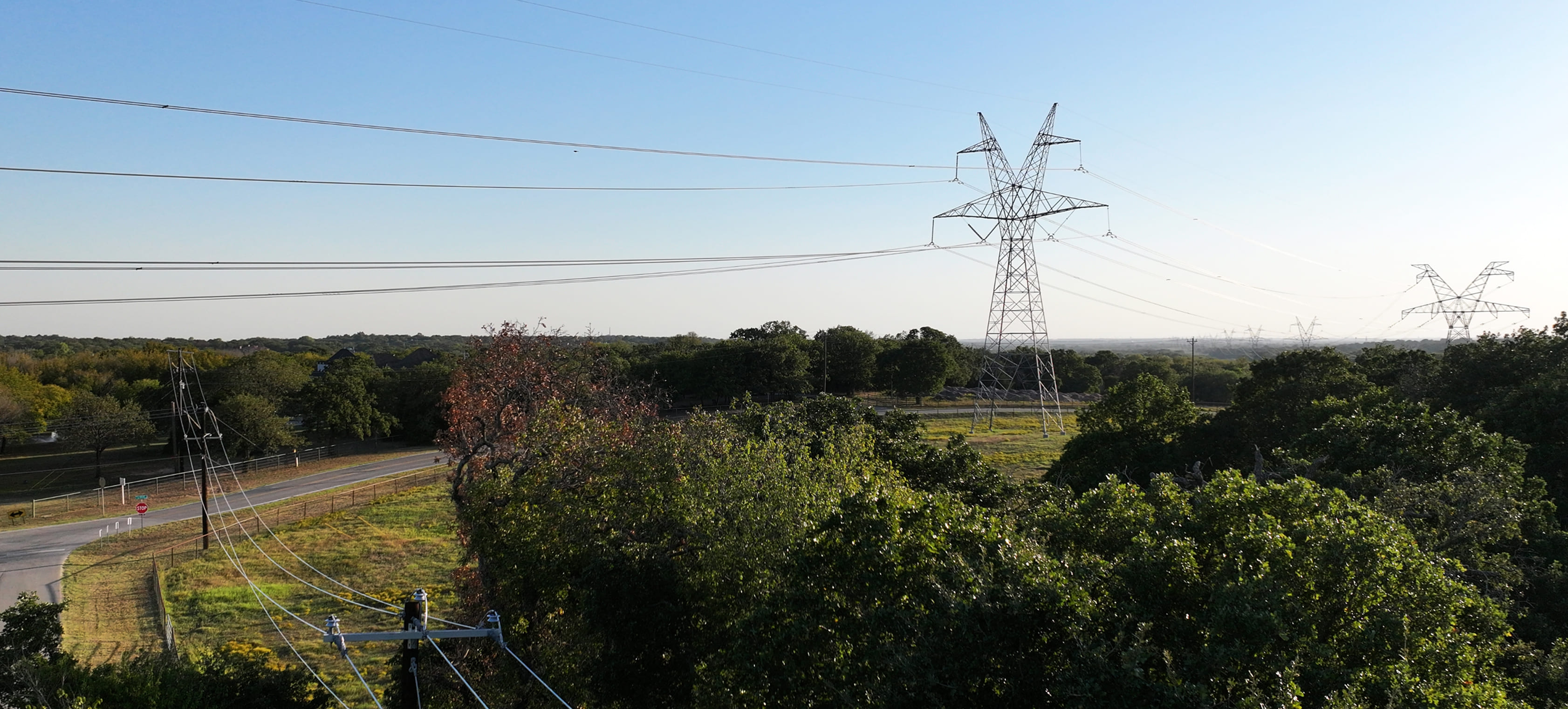 High-voltage power lines stretching across a forested landscape under a blue sky