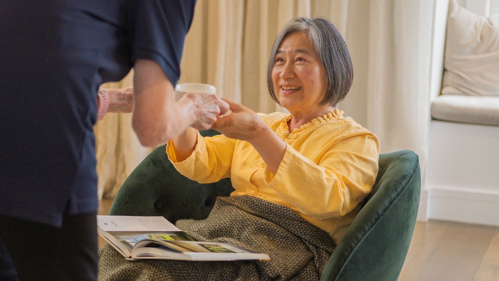 Woman accepting a hot drink from a home care worker