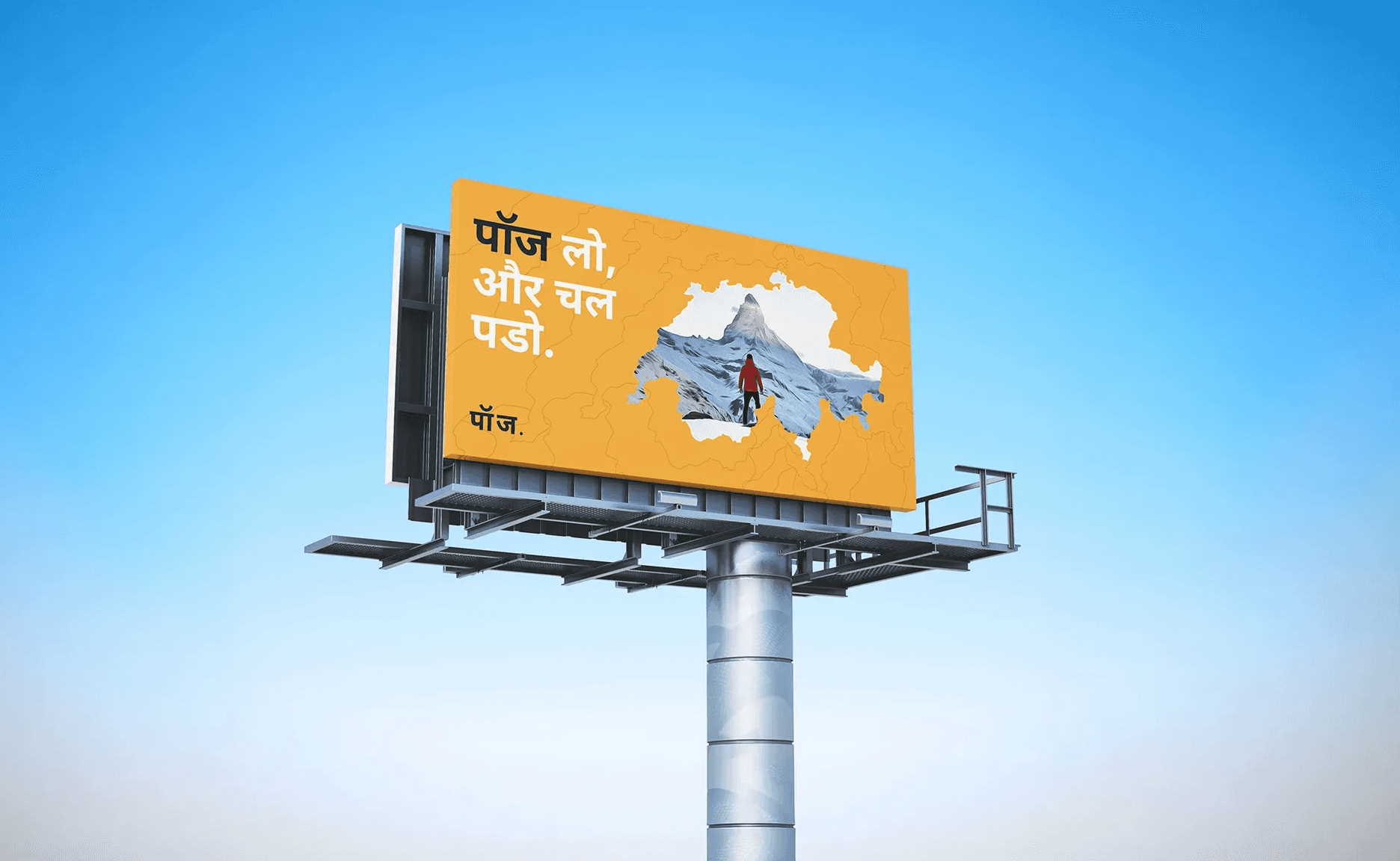 Orange Hindi-language billboard on a tall metal pole, featuring bold text, a map graphic, and a mountain image against a clear blue sky.