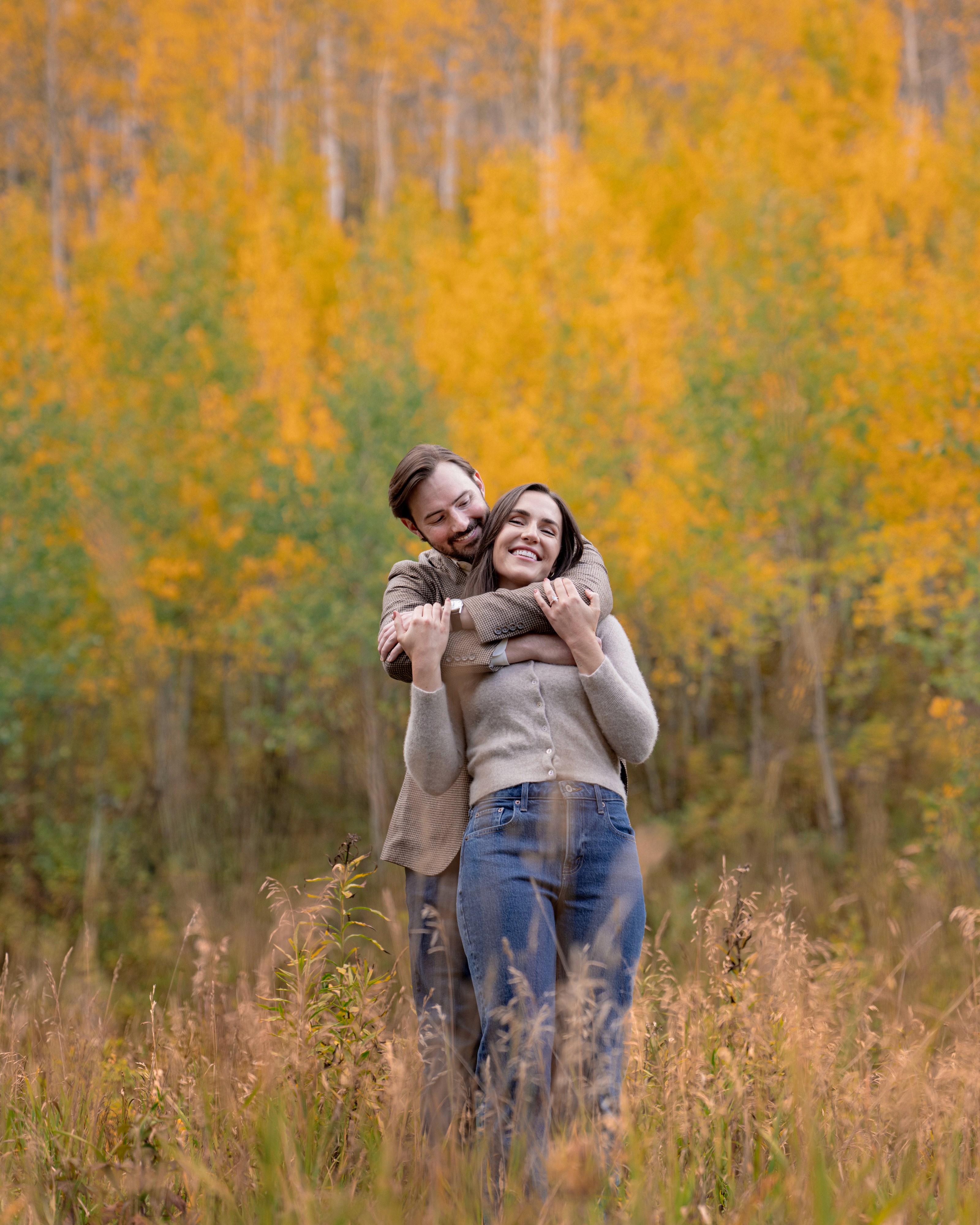 Tim embraces Lexi from behind as she smiles among autumn aspens.