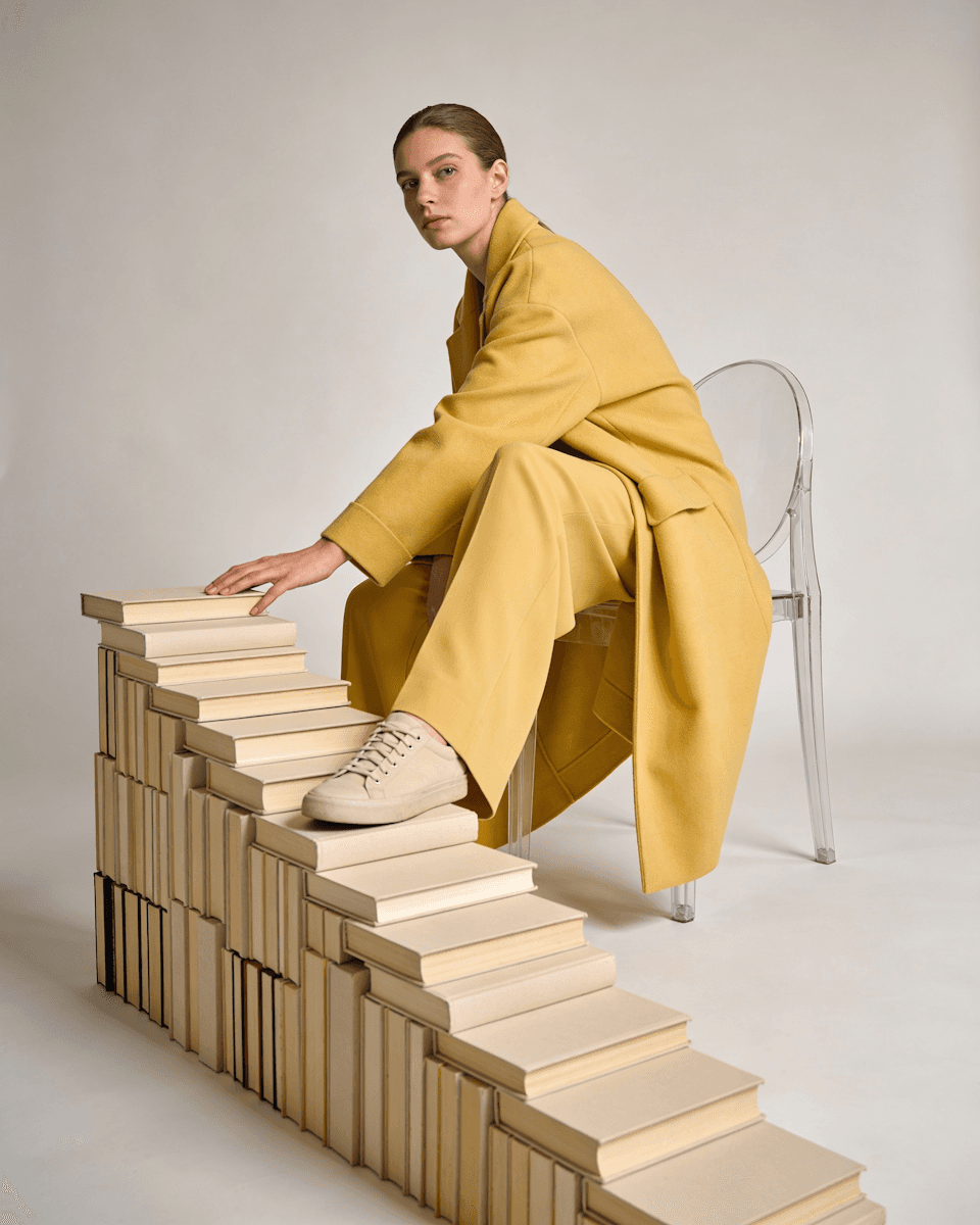 A woman sitting with one foot on a pile of books.