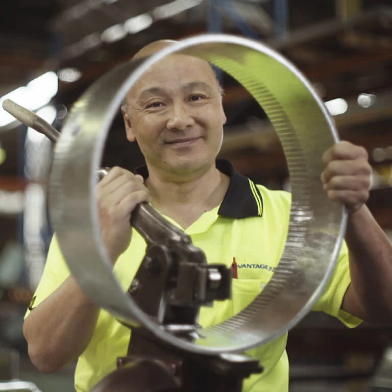 A MyPlace team member smiling while inspecting a manufactured component, representing MyPlaceIQ’s commitment to Australian-designed and Australian-made smart home products.