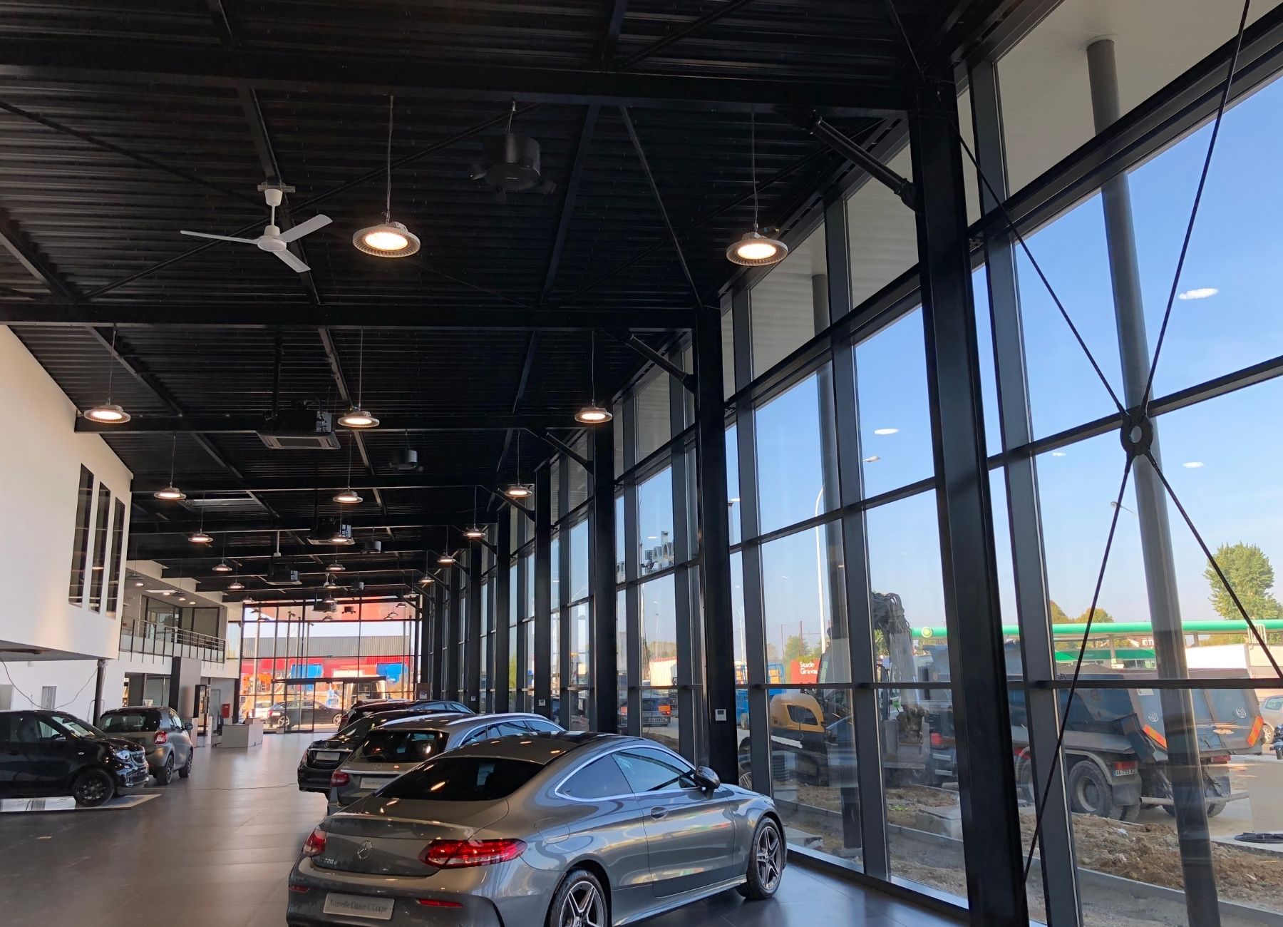 Vue intérieure d’un showroom automobile avec grandes baies vitrées et structure métallique apparente.