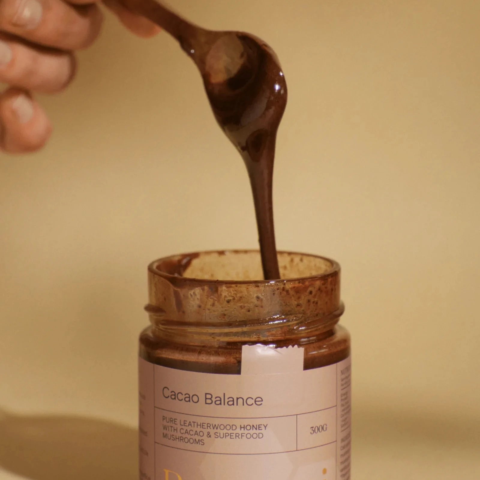 Jar of Beeburni Cacao Balance spread with a hand using a spoon to scoop out the chocolate spread.