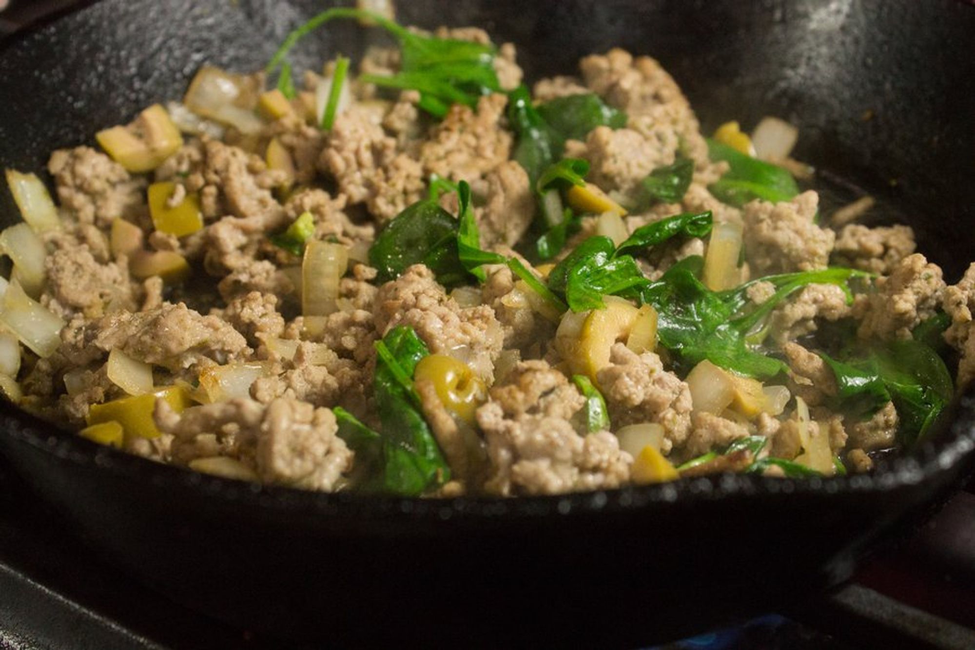 chicken with garlic, onion, olives, oregano, and spinach in a pan