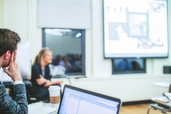 A photo of a group of people listening to a lecture and watching a screen projector.