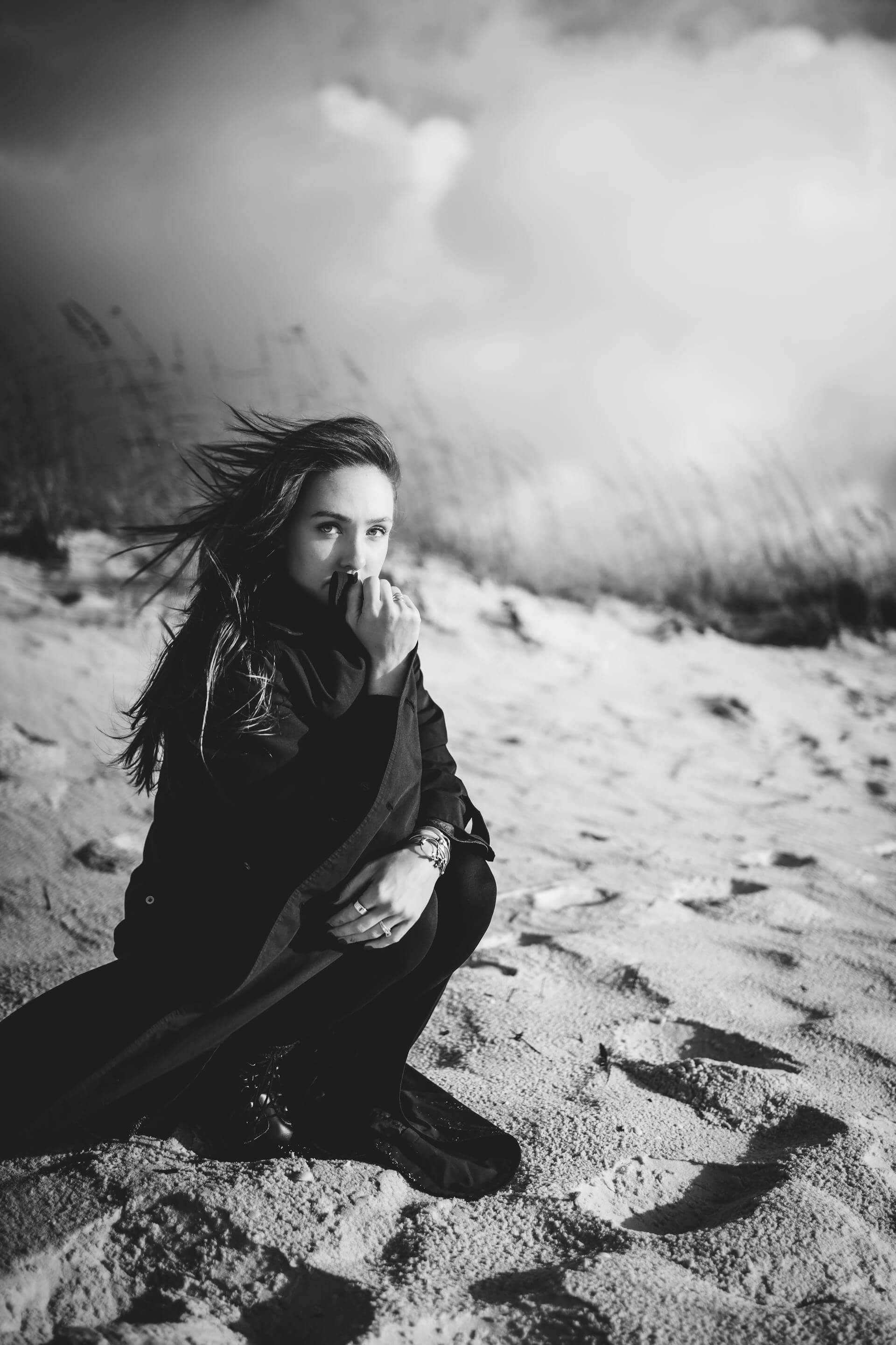 A woman sits on the beach, resting her chin on her hand, gazing thoughtfully at the ocean waves